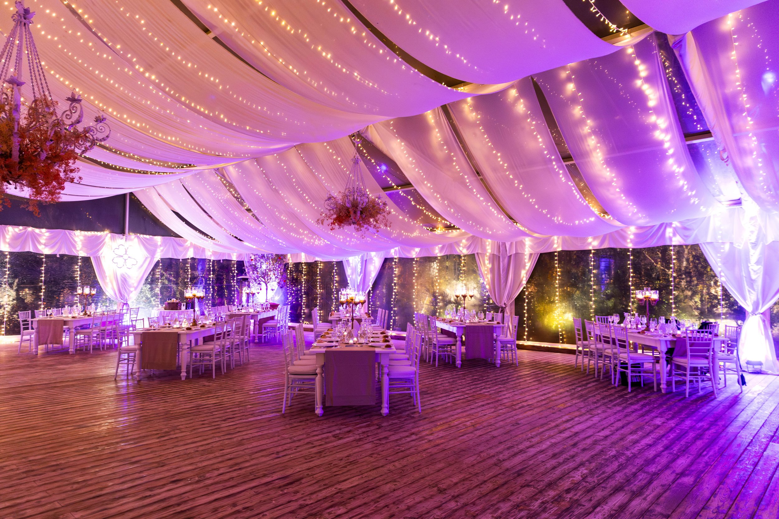 Interno di una sala per eventi in Valle d'Itria decorata con luci soffuse e tende bianche, tavoli apparecchiati per cena.
