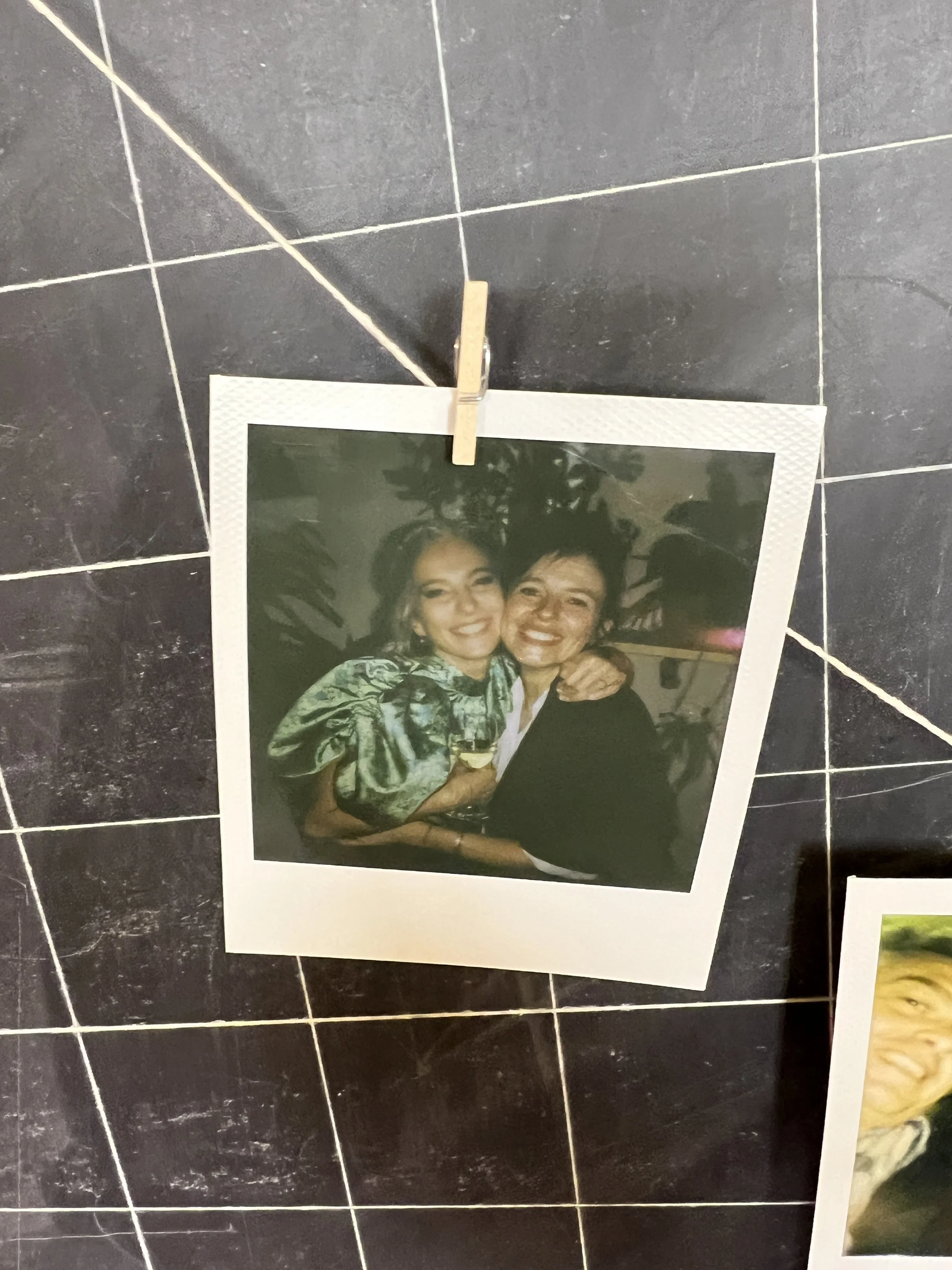 Foto Polaroid di due persone sorridenti abbracciate, attaccata a una lavagna con una molletta di legno.