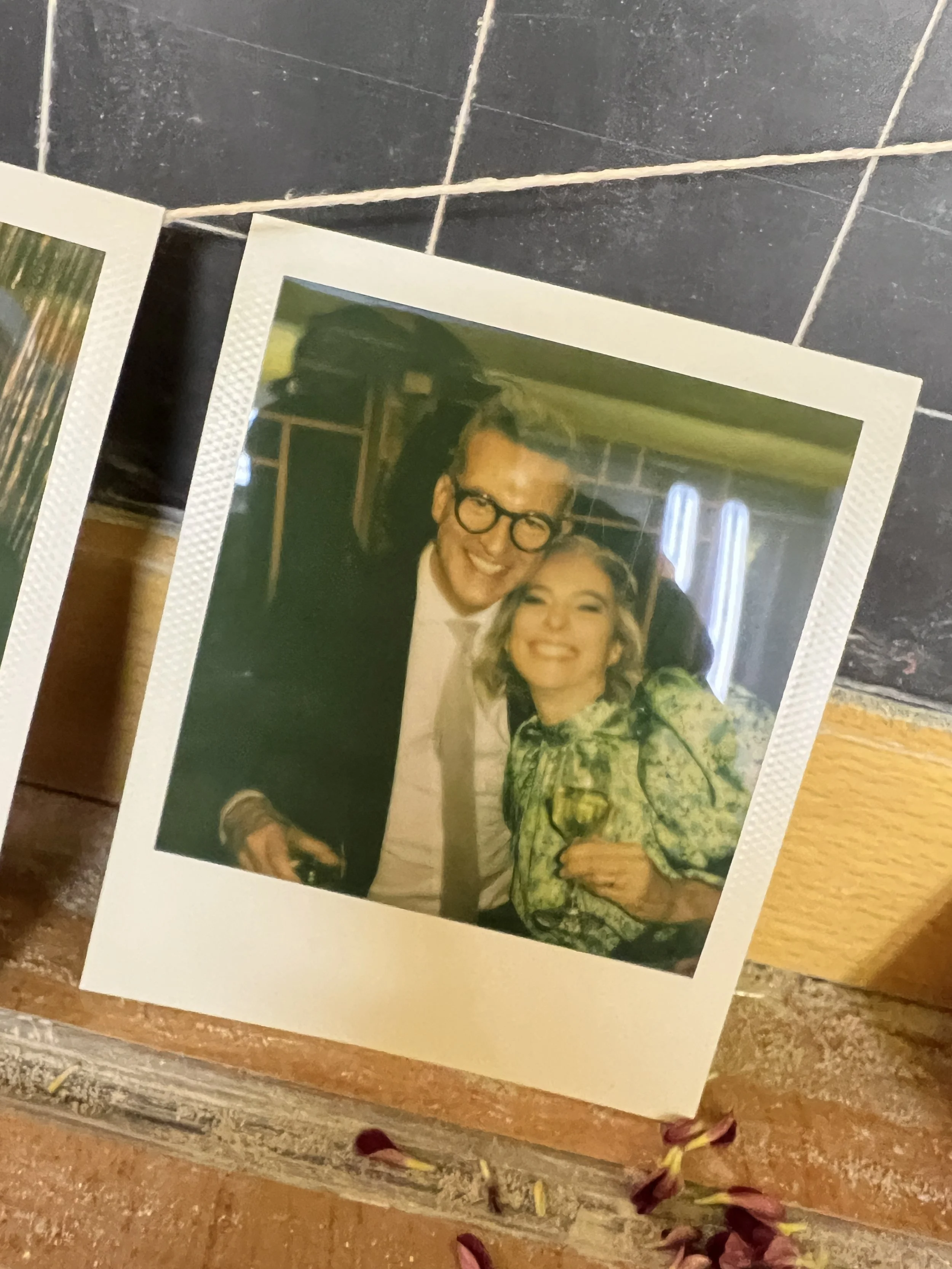 Due persone sorridenti posano per una foto Polaroid, una tiene un bicchiere di vino. Stanno festeggiando il loro matrimonio.