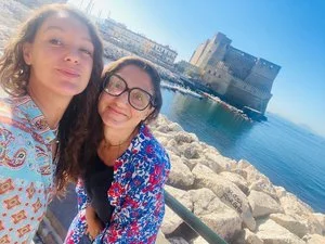 Due persone sorridenti su un lungomare con il Castel dell'Ovo sullo sfondo a Napoli, Italia.