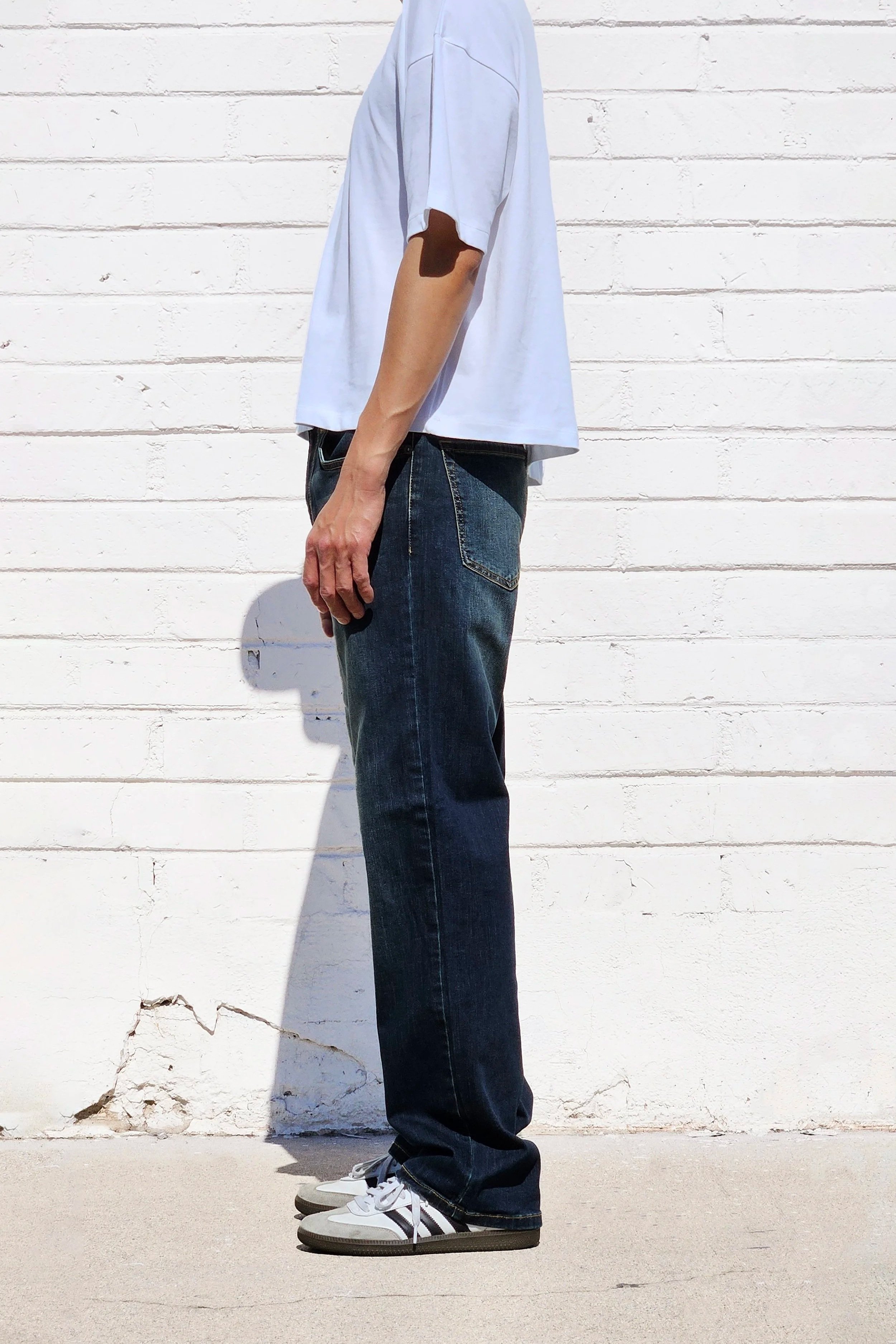 Side view of model in mens dark indigo faded jeans relaxed straight 90s fit.
