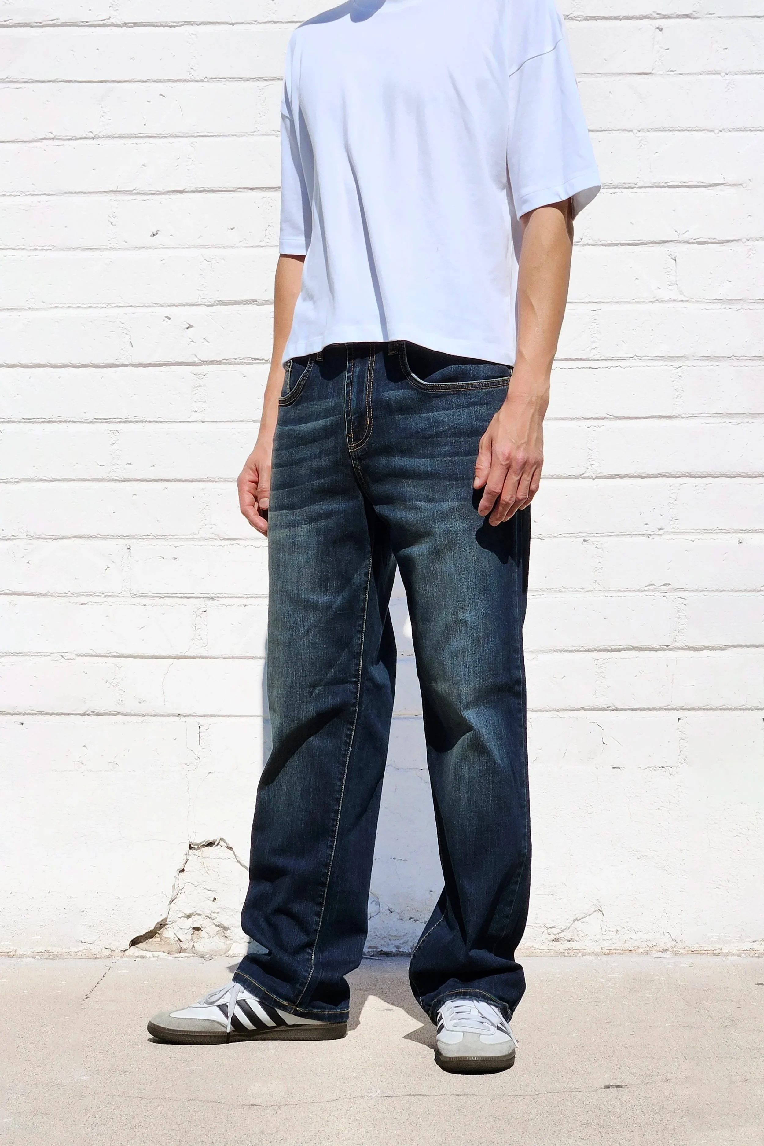 Side view of model in mens dark indigo faded jeans relaxed straight 90s fit.