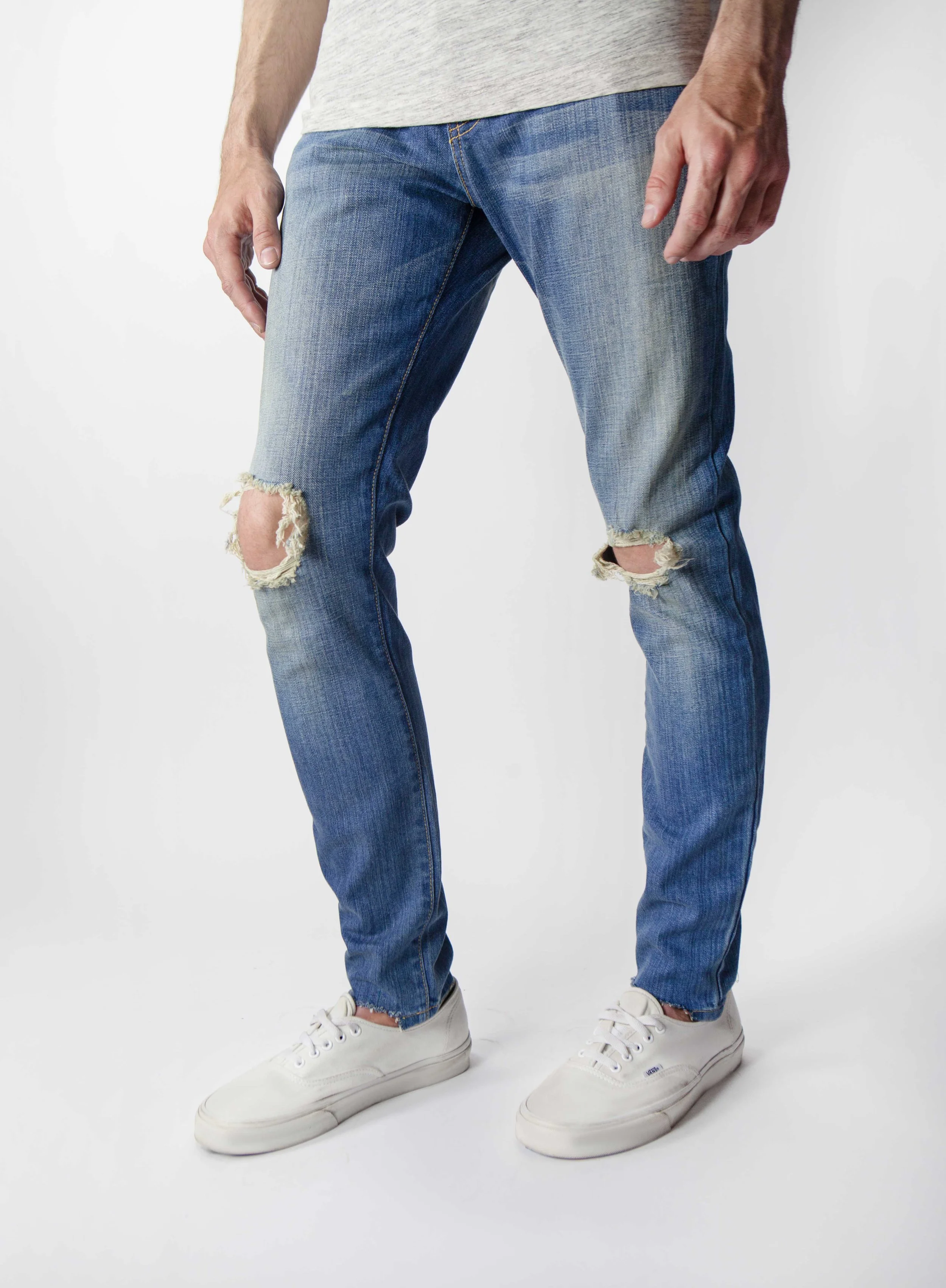 Side view of model in men’s medium blue ripped skinny jeans.