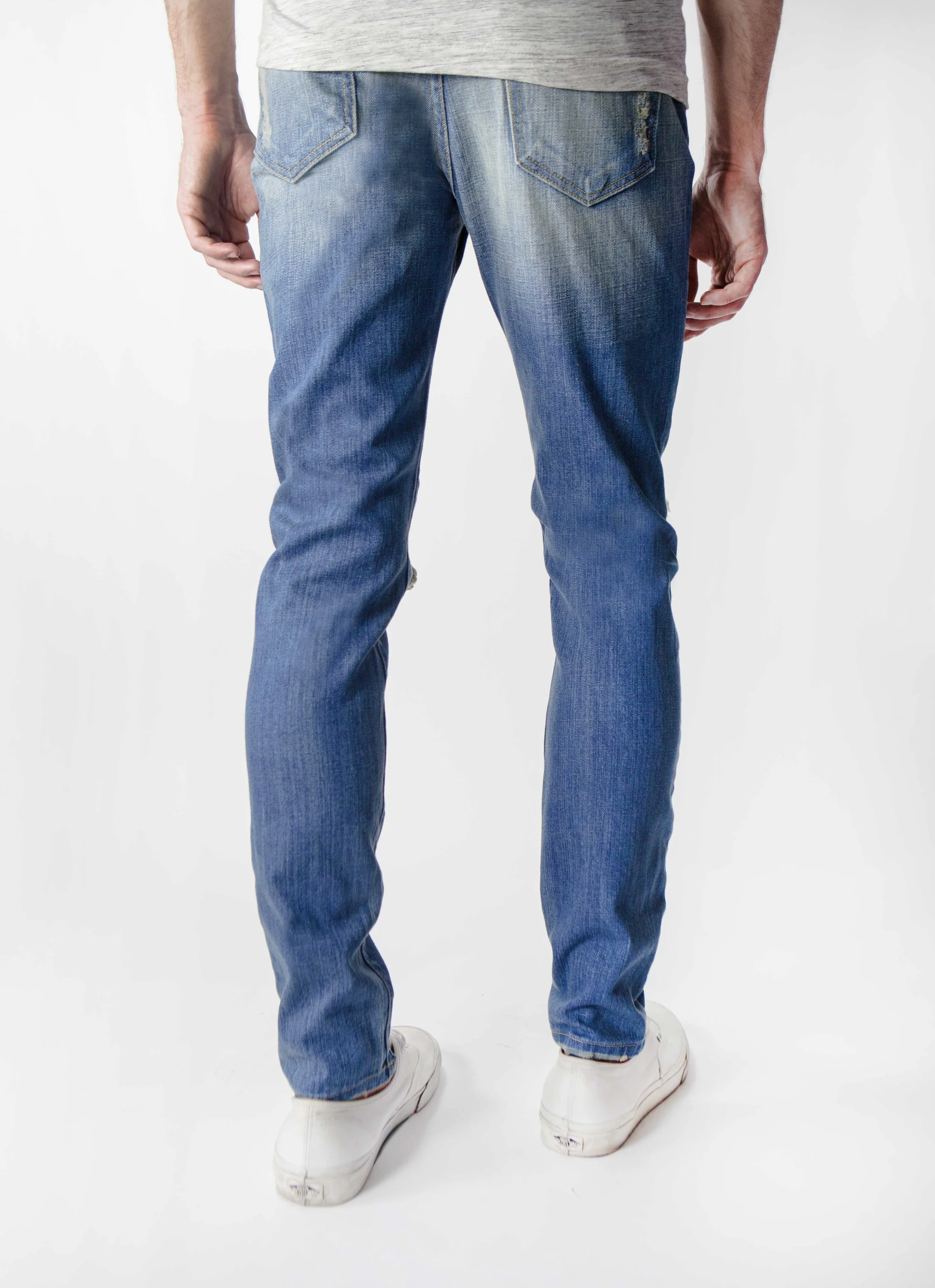 Back view of model in men’s medium blue ripped skinny jeans.
