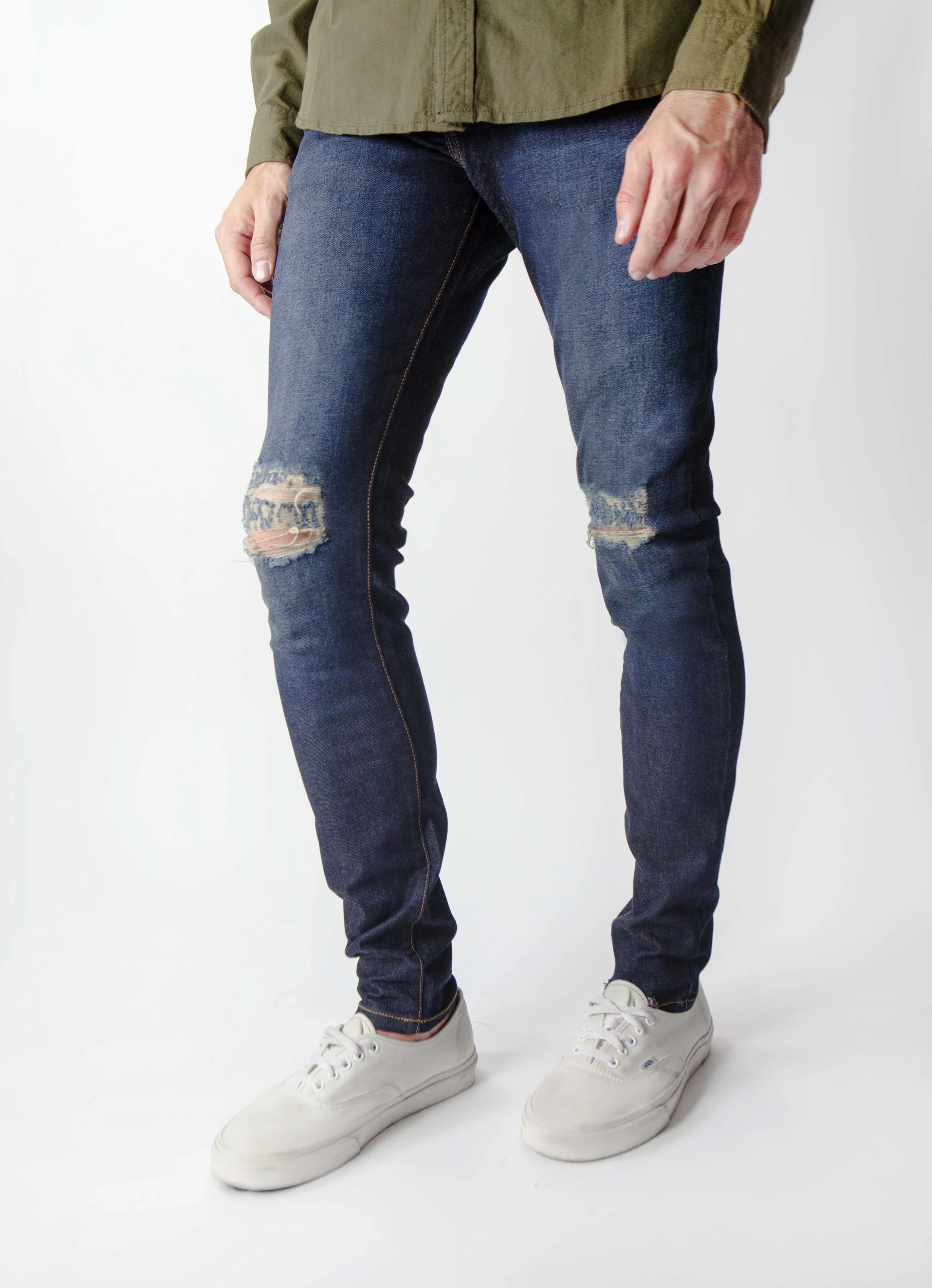 Side view of model in men’s indigo blue ripped skinny jeans.