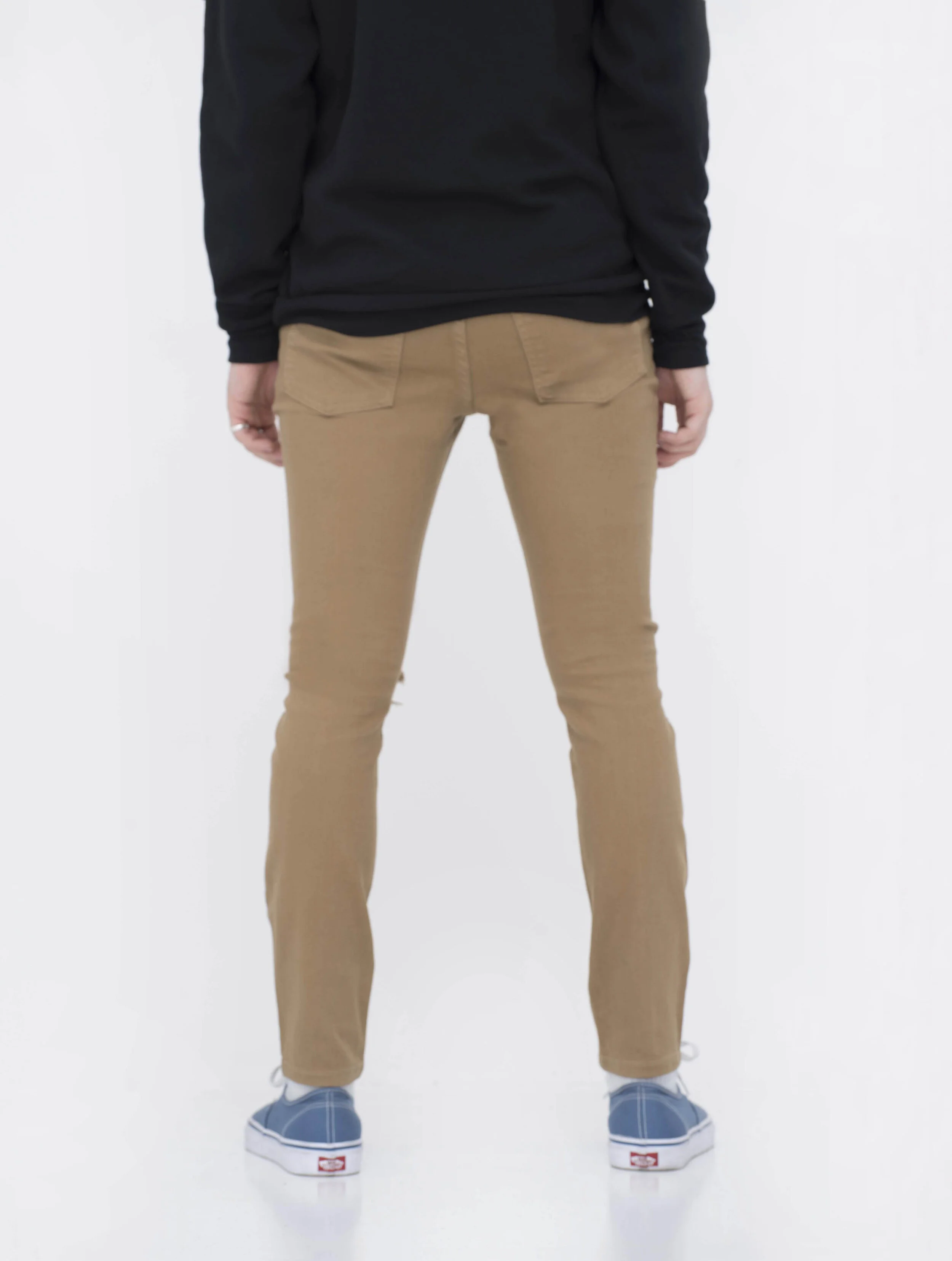 Back view of model in men’s knee ripped camel skinny jeans.