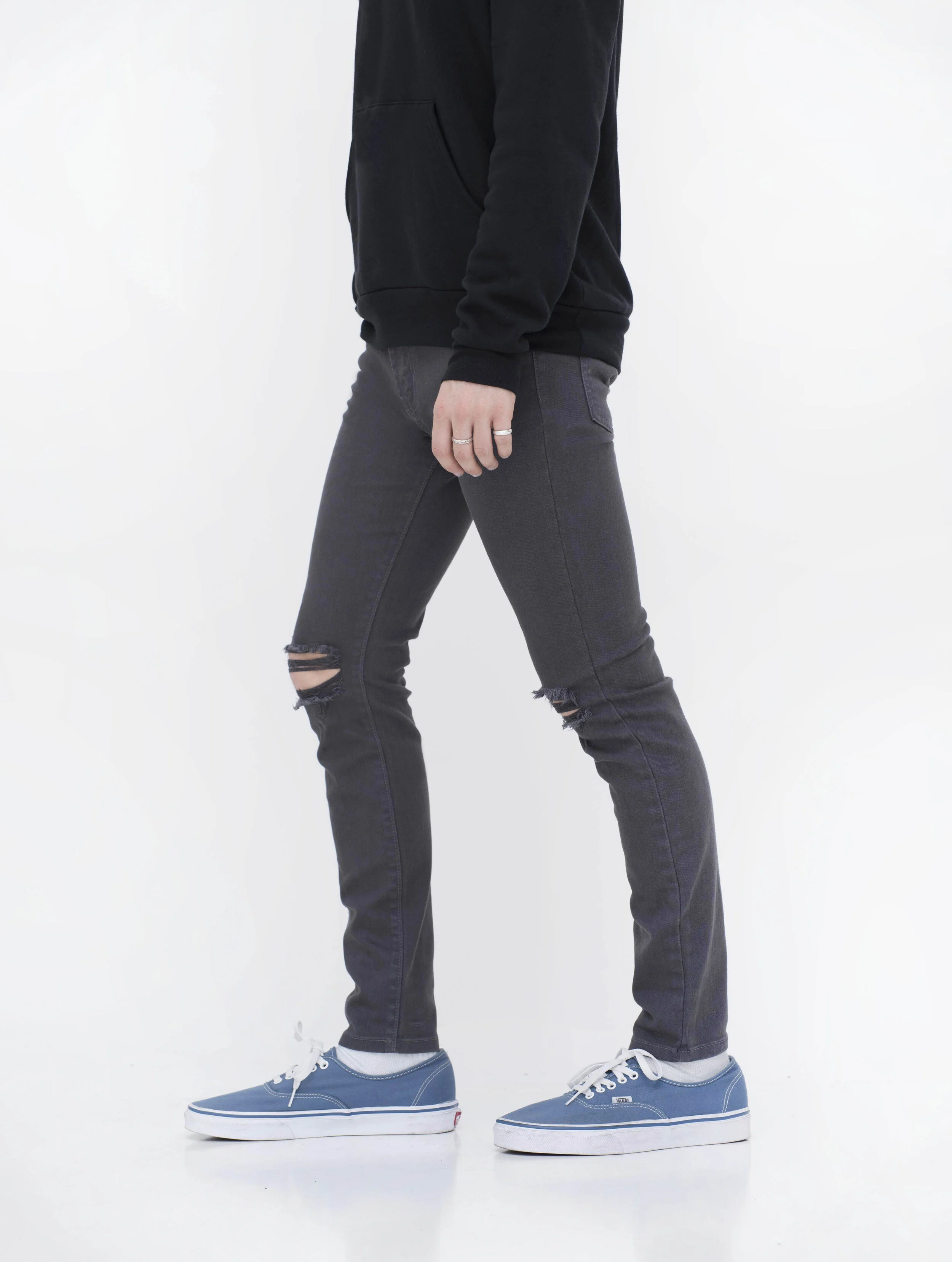Side view of model in men’s knee ripped charcoal skinny jeans.