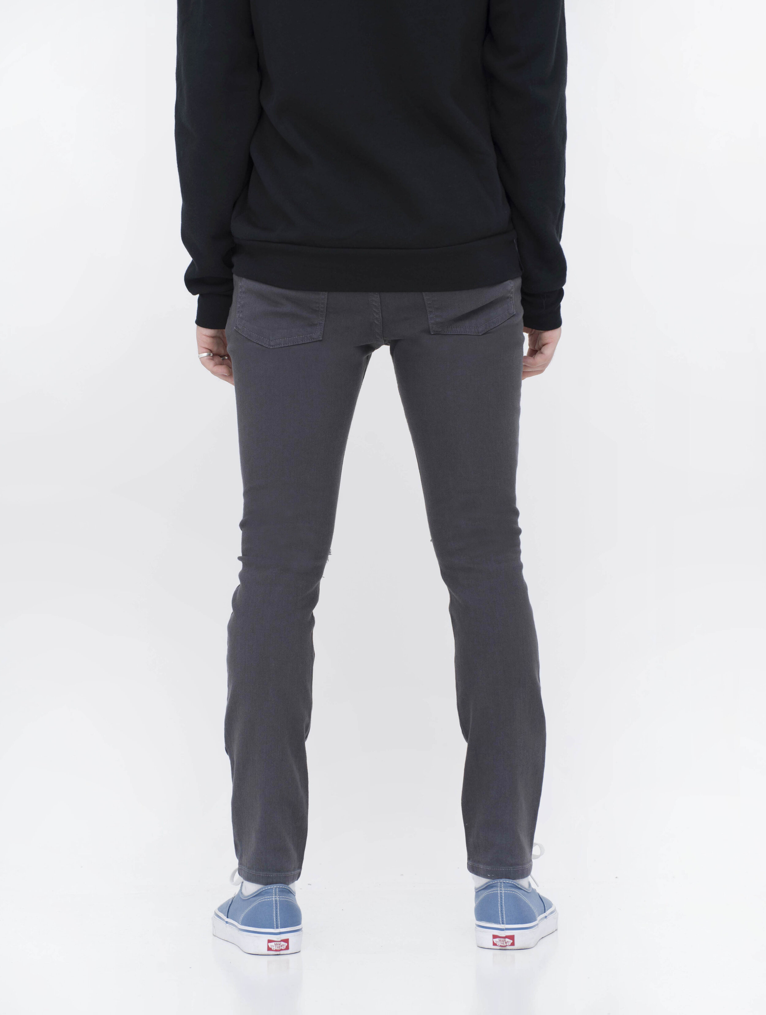 Back view of model in men’s knee ripped charcoal skinny jeans.