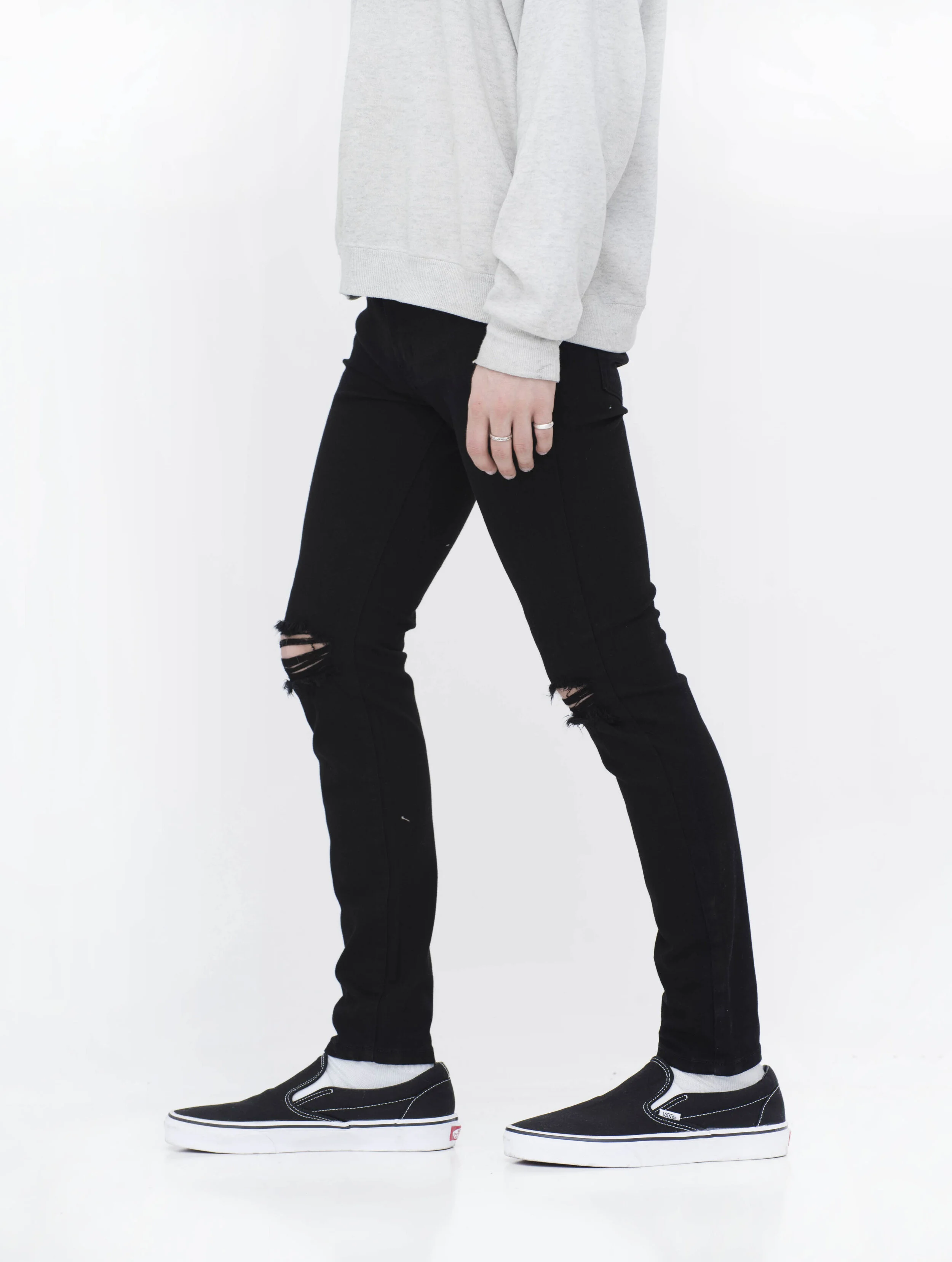 Side view of model in men’s knee ripped black skinny jeans.