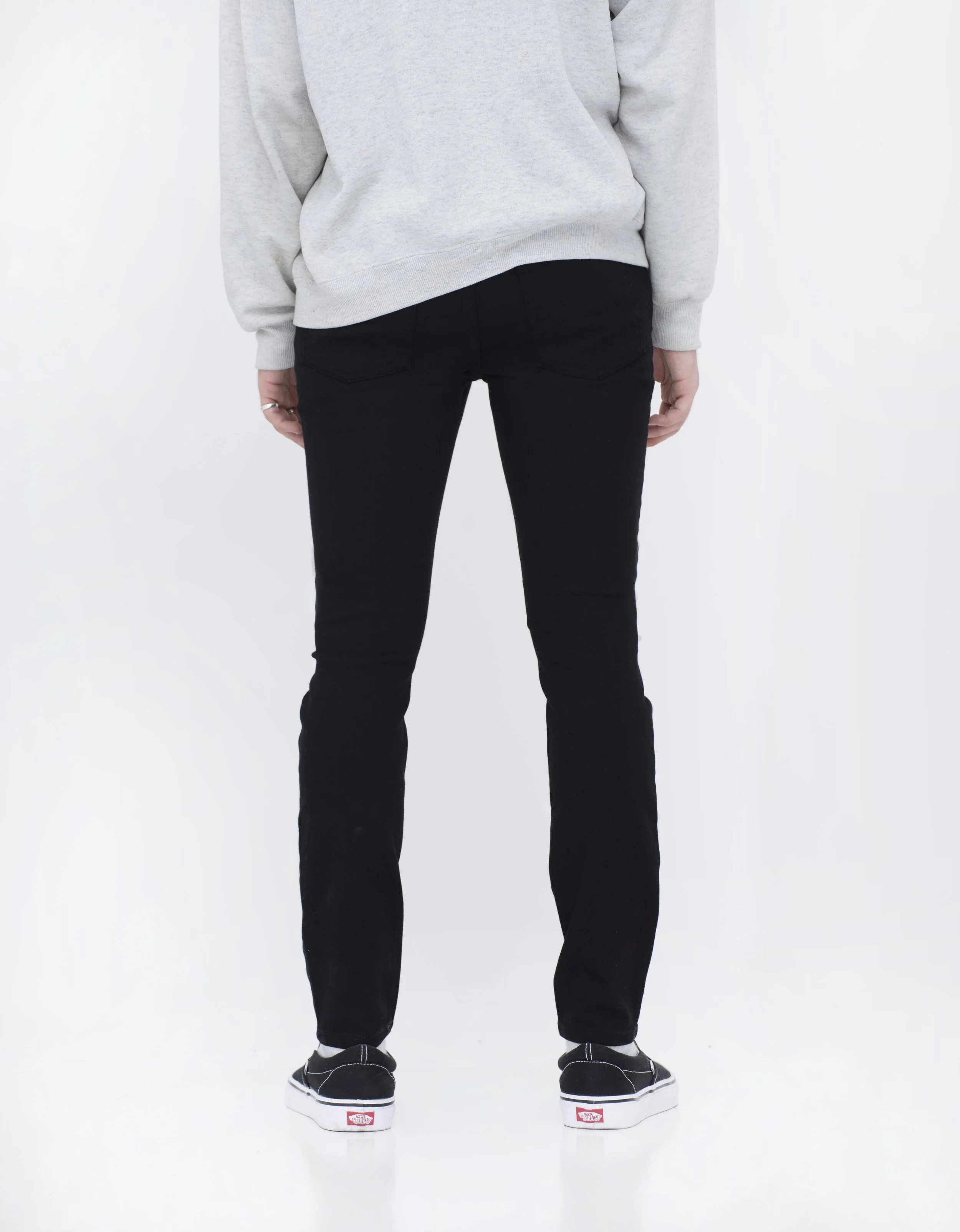 Back view of model in men’s knee ripped black skinny jeans.