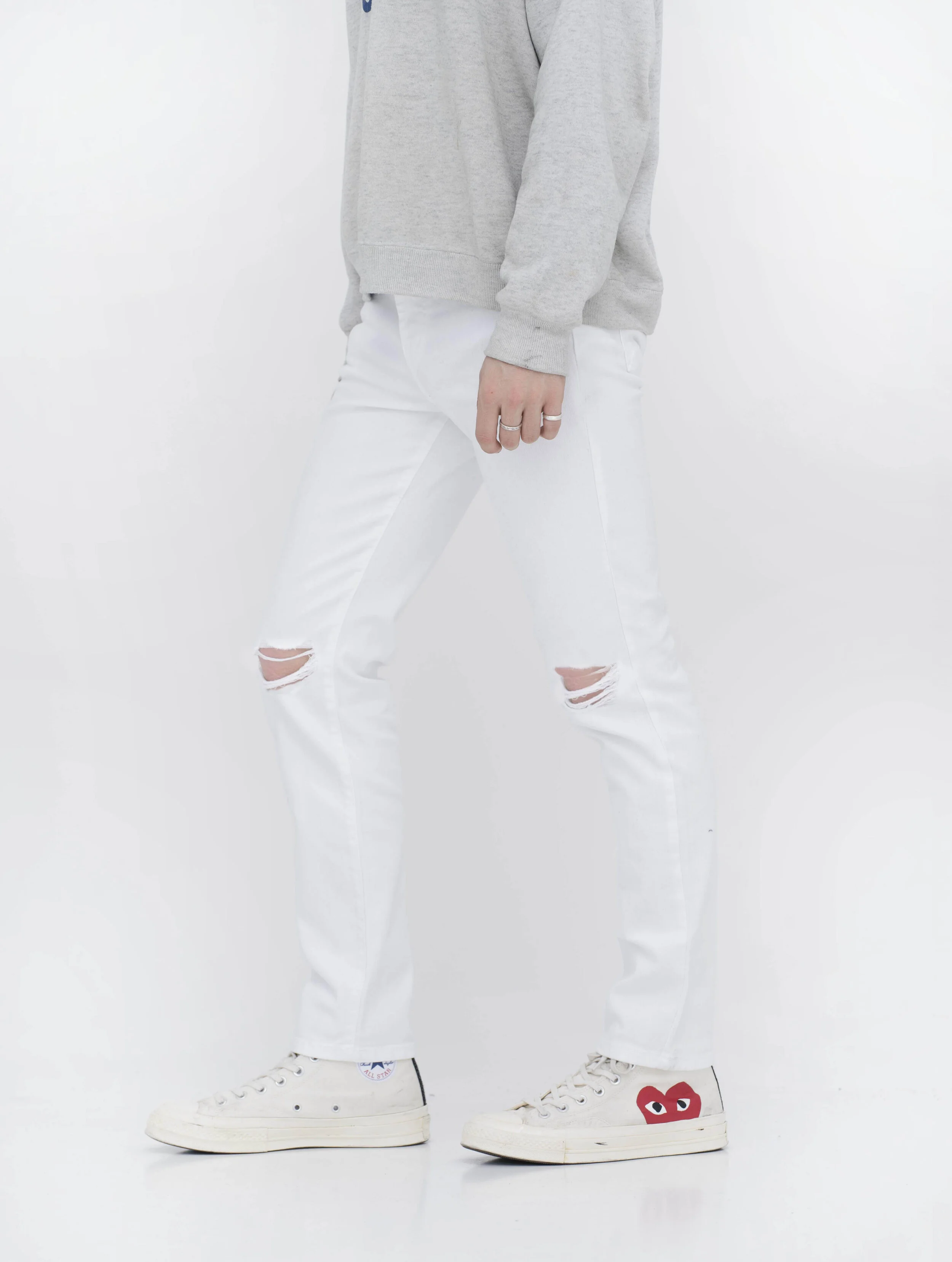 Side view of model in men’s knee ripped white skinny jeans.