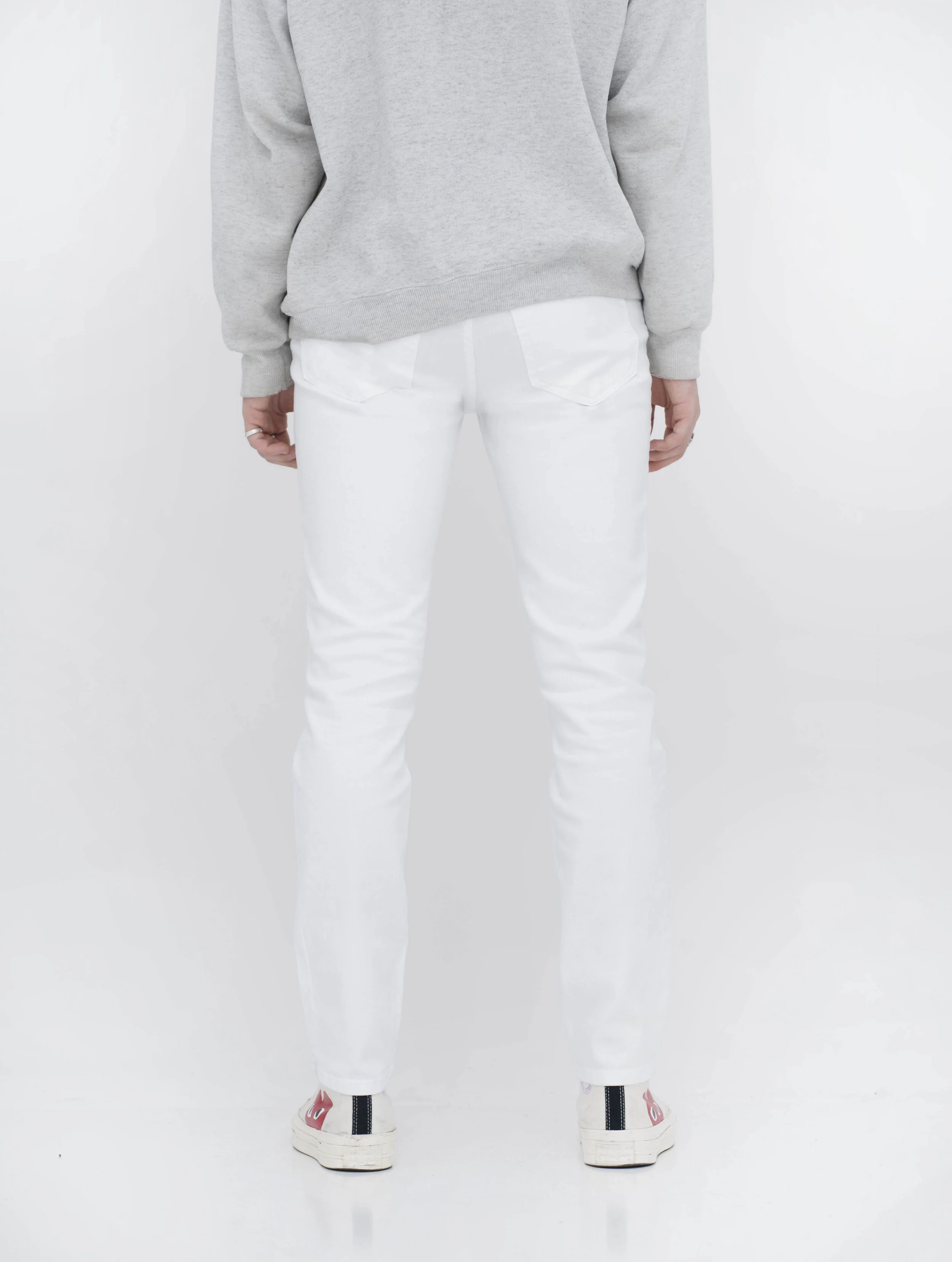 Back view of model in men’s knee ripped white skinny jeans.