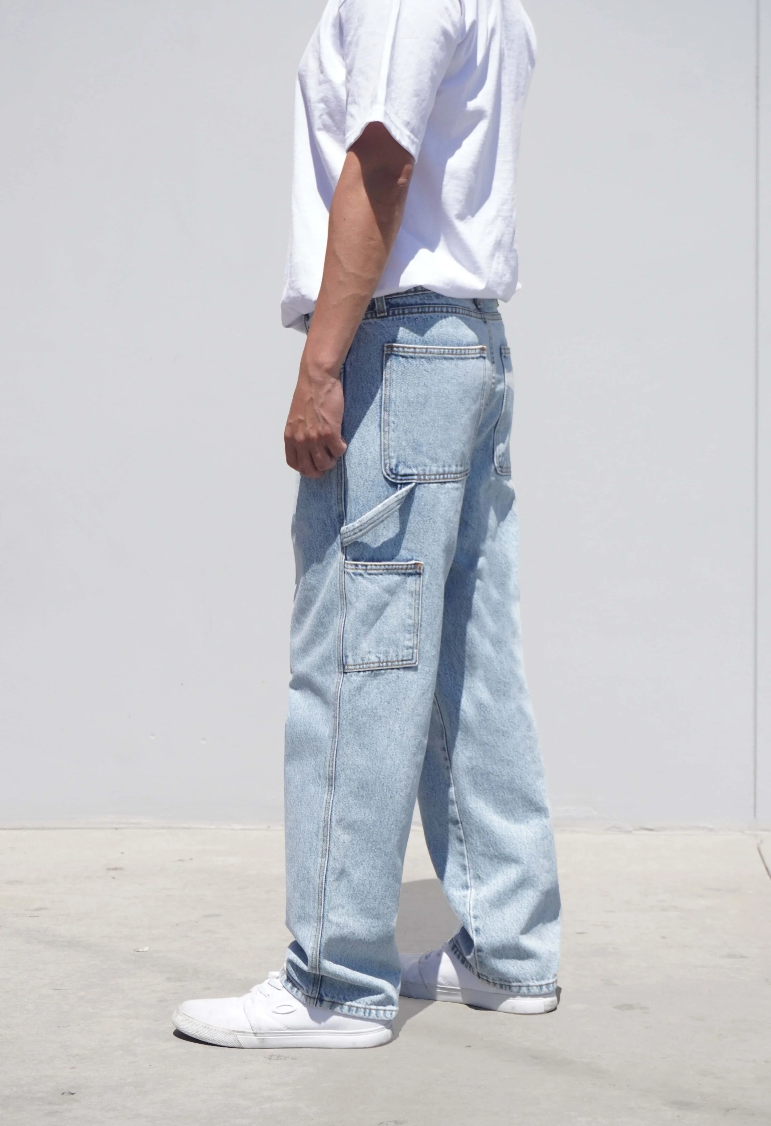 Side view of model in pastel blue denim baggy carpenter jeans.