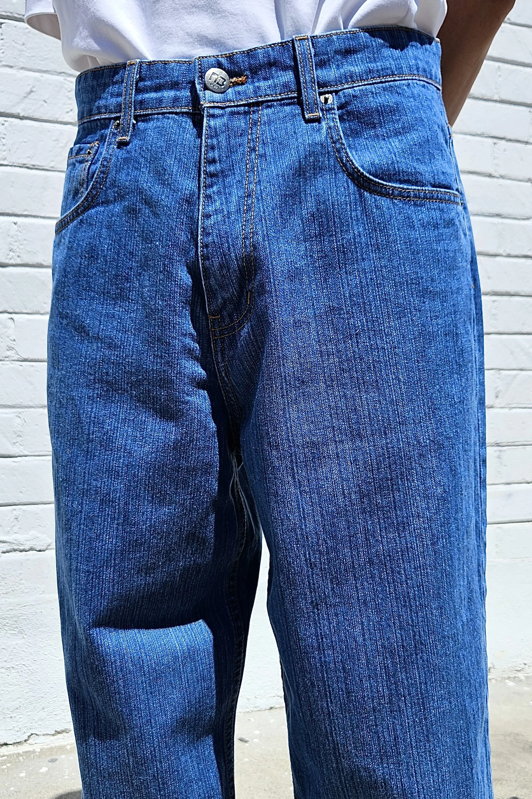 Close up view of model in men’s medium blue baggy slub denim jeans.