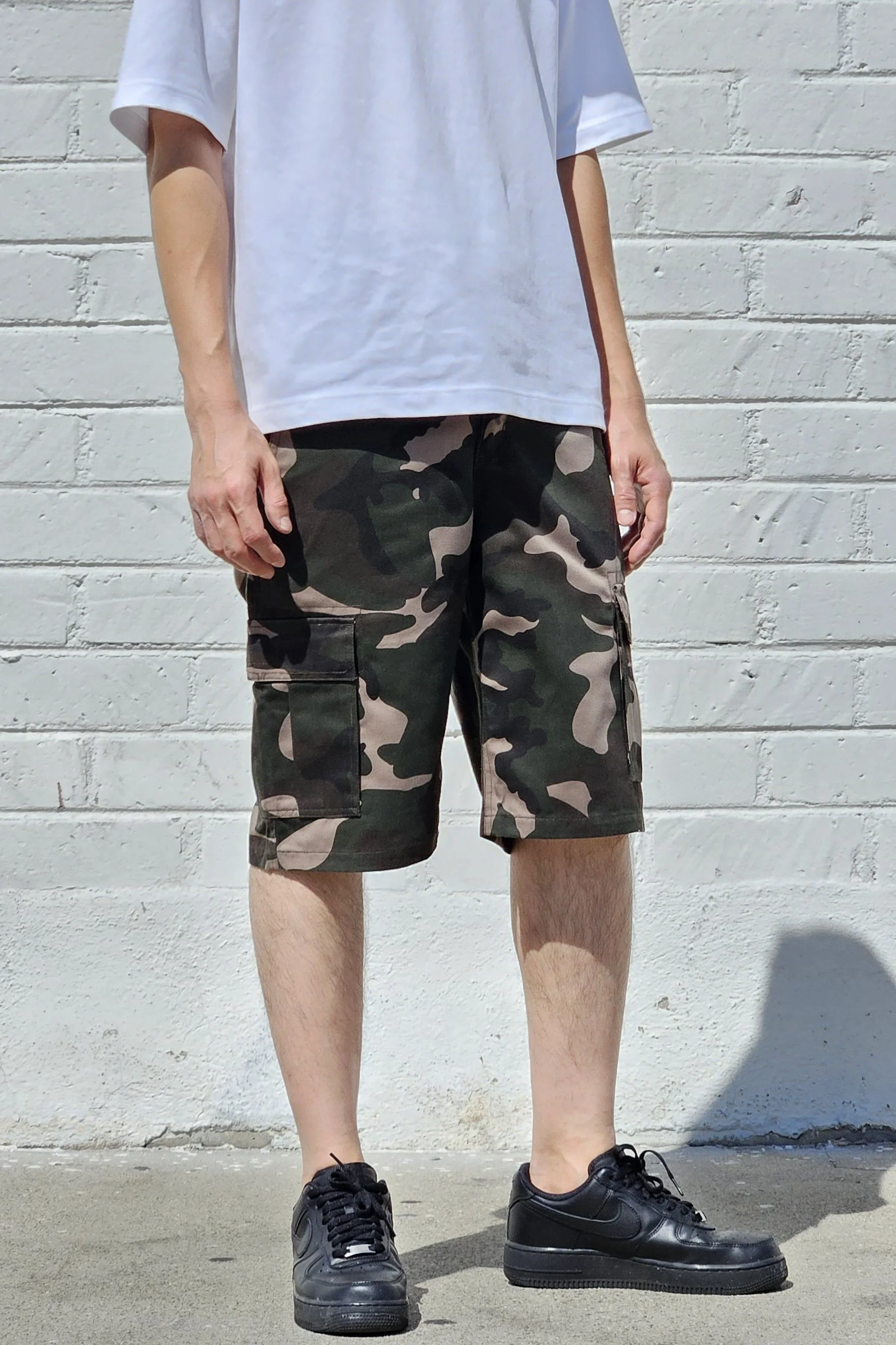 Front side view of model in camo green cargo baggy shorts.