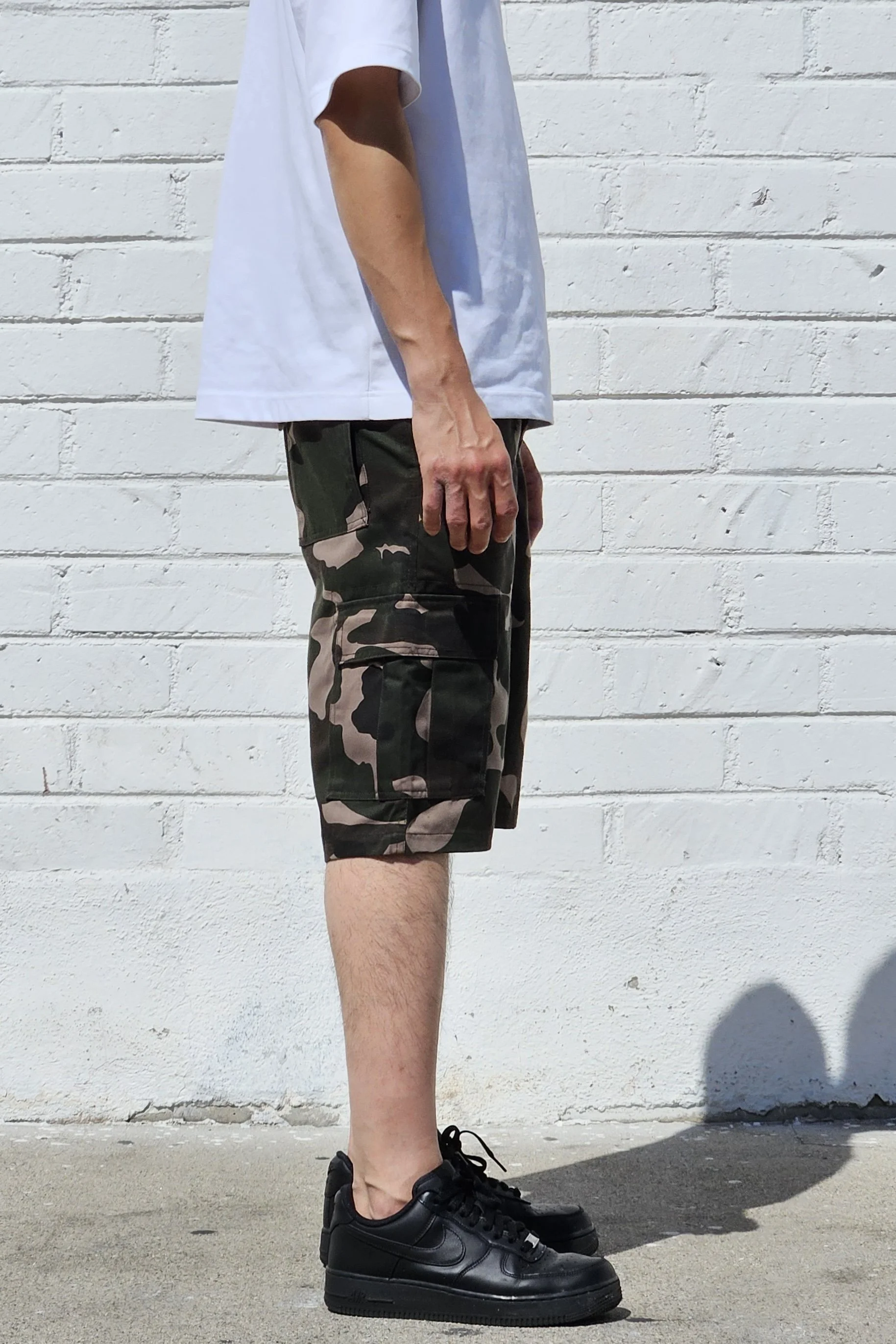 Side view of model in camo green cargo baggy shorts.