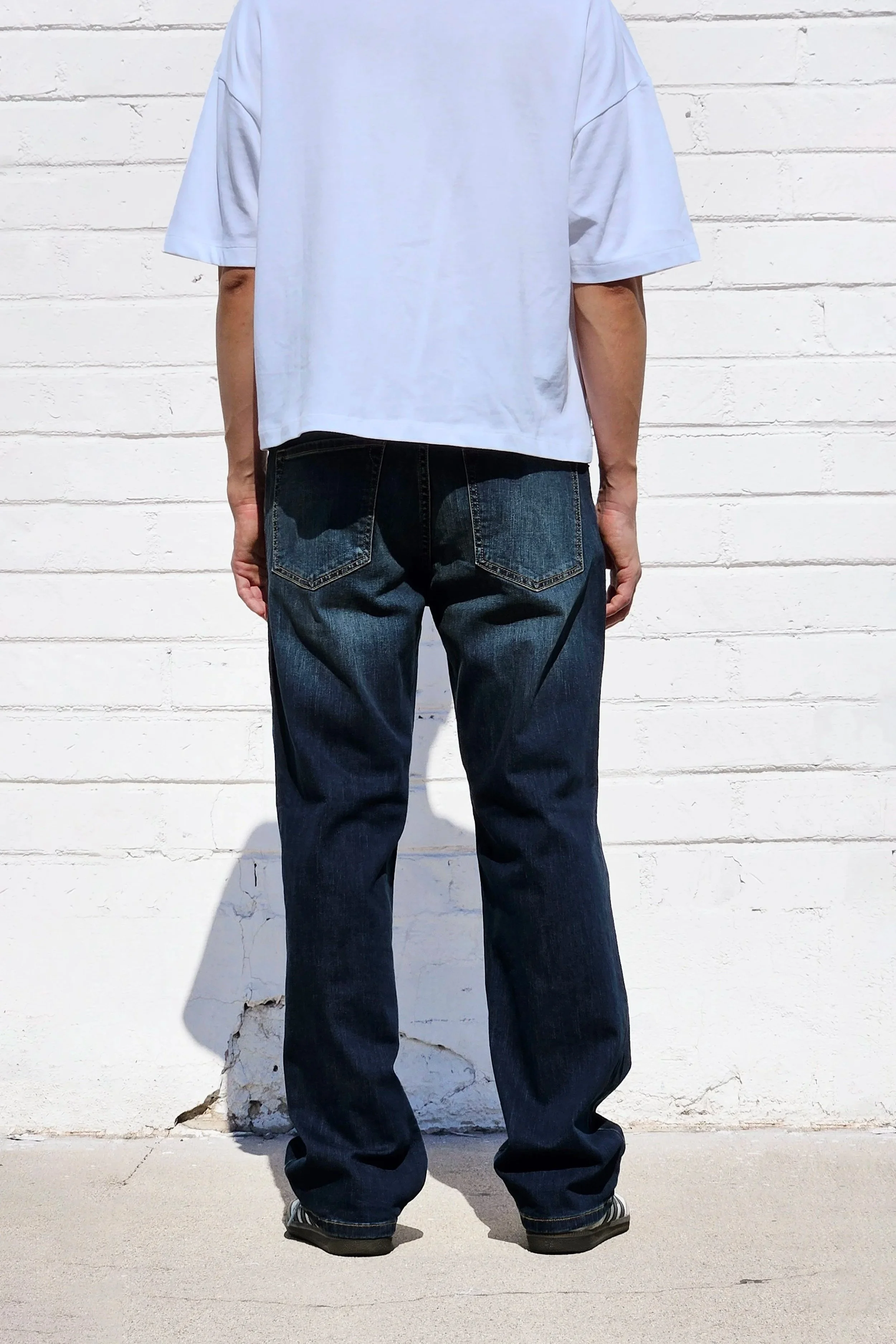 Back view of model in mens dark indigo faded jeans relaxed straight 90s fit.