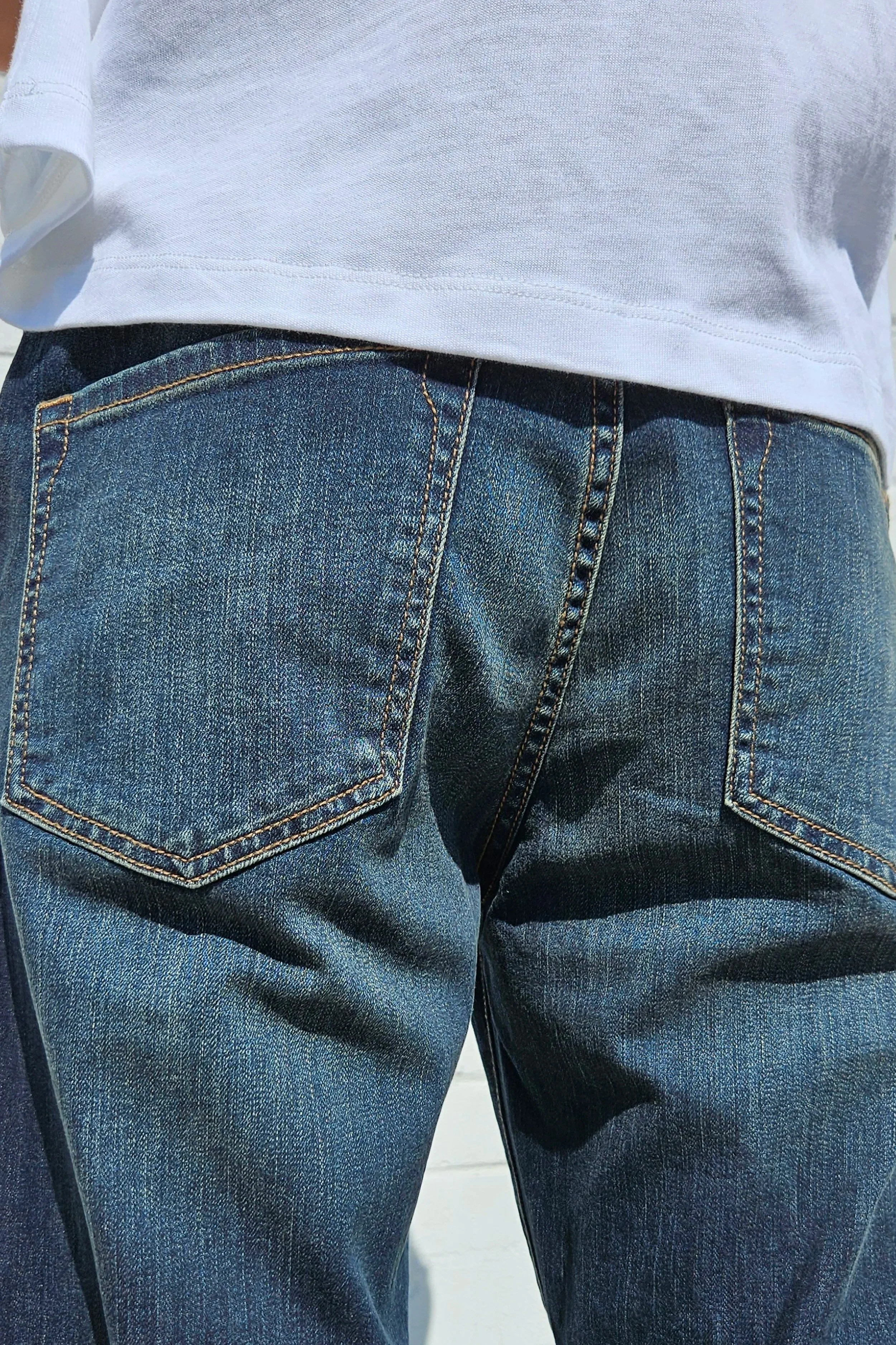 Detail back view of model in mens dark indigo faded jeans relaxed straight 90s fit.