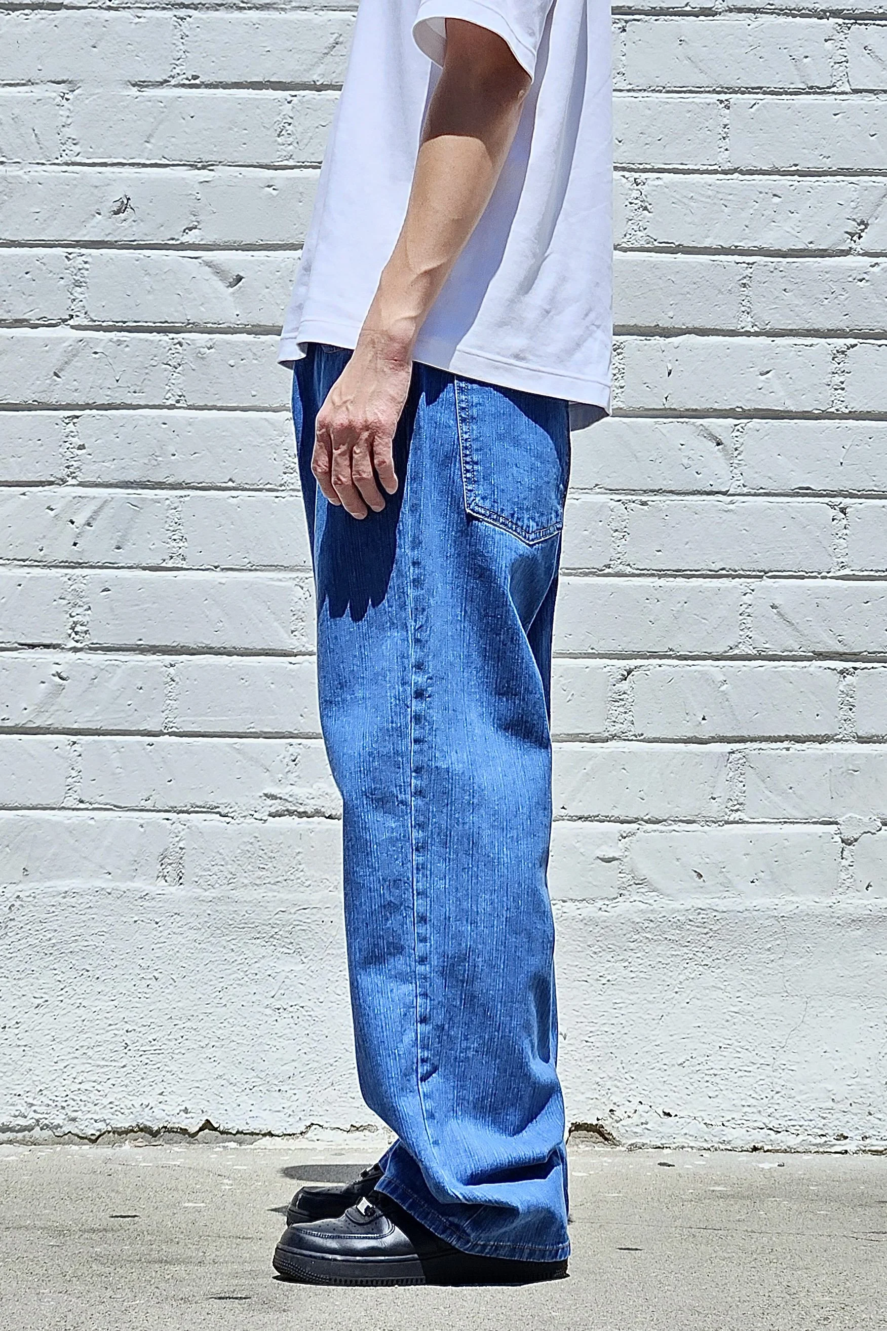 Side view of model in men’s medium blue baggy slub denim jeans.