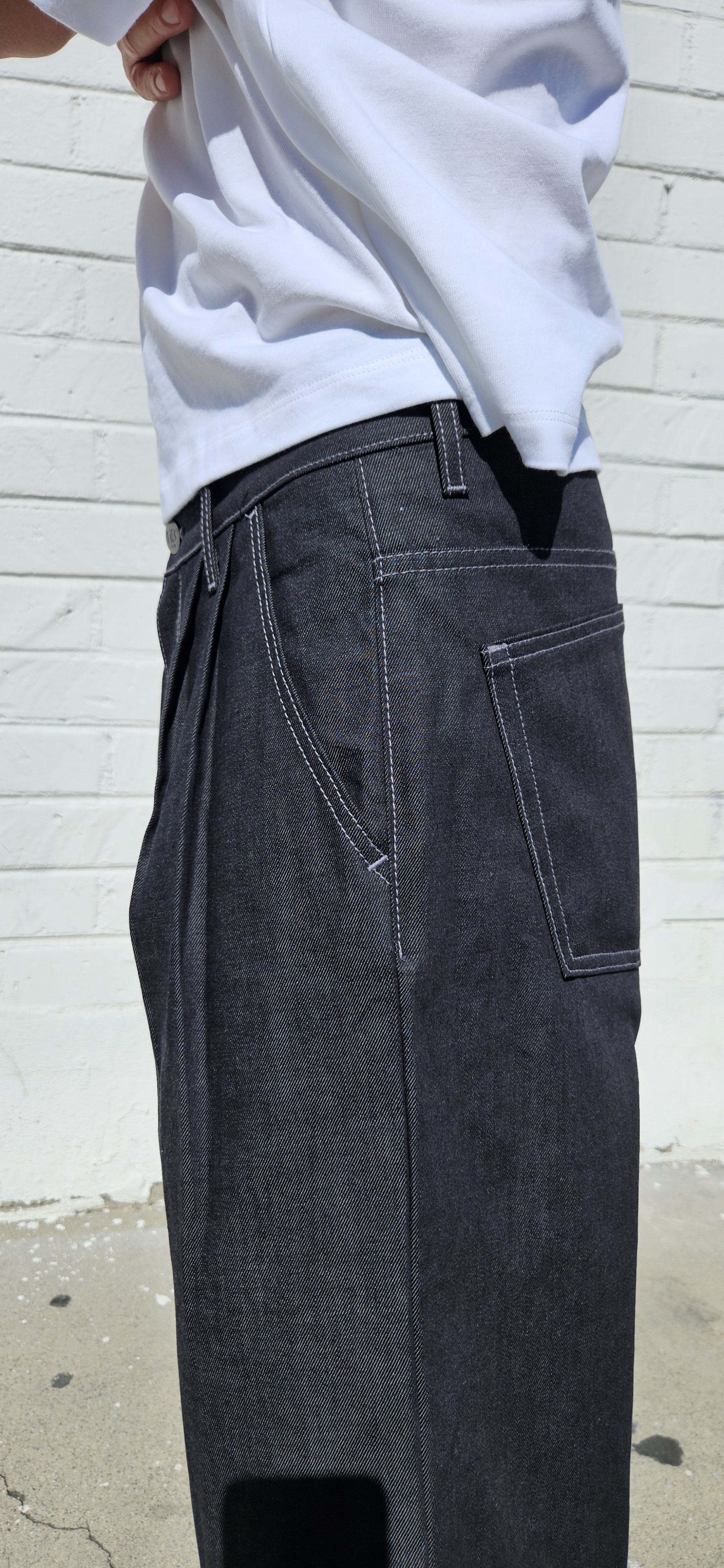 Side close up view of denim charcoal double pleated baggy jean short with d-ring attachment