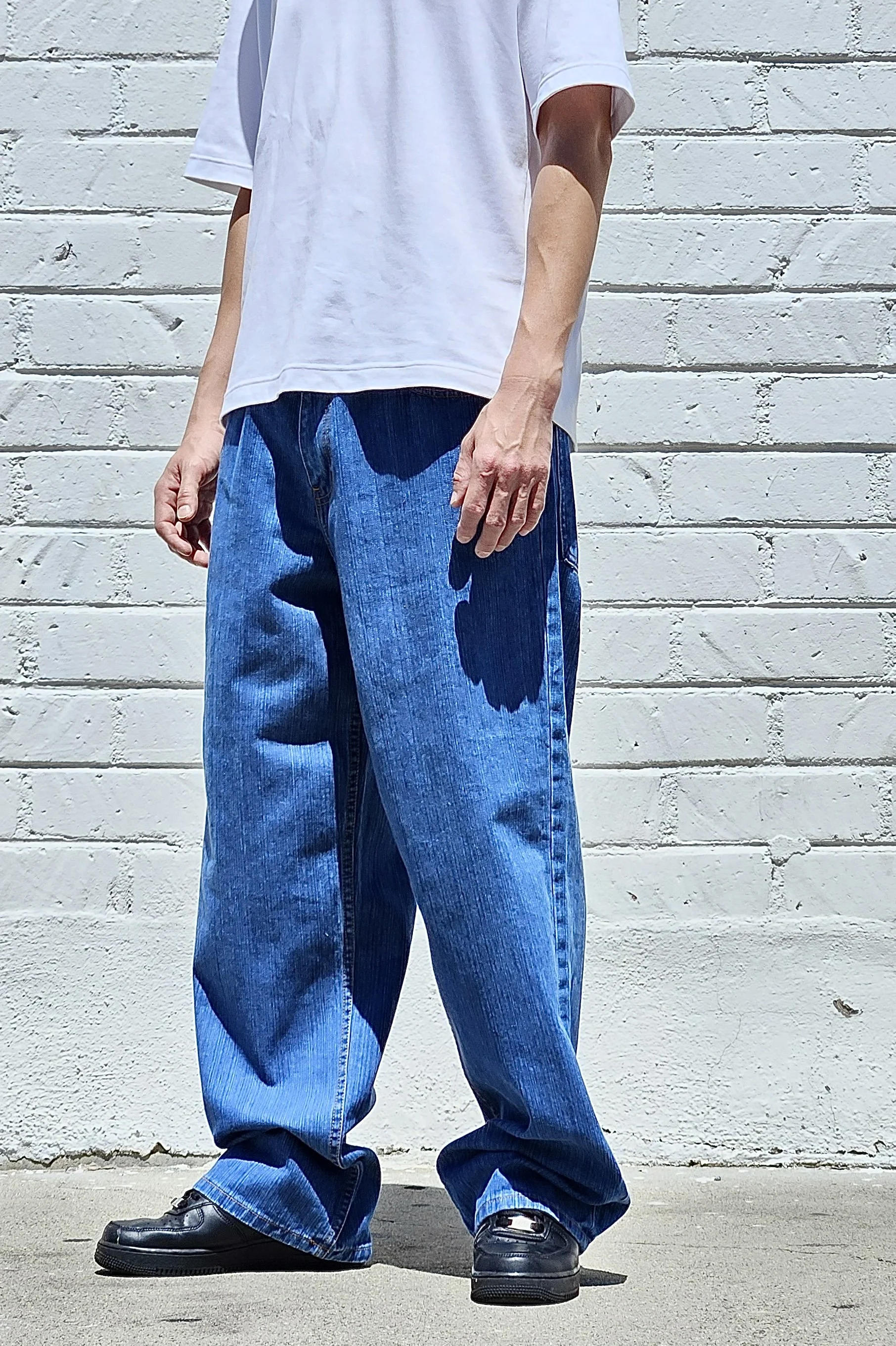 Side view of model in men’s medium blue baggy slub denim jeans.