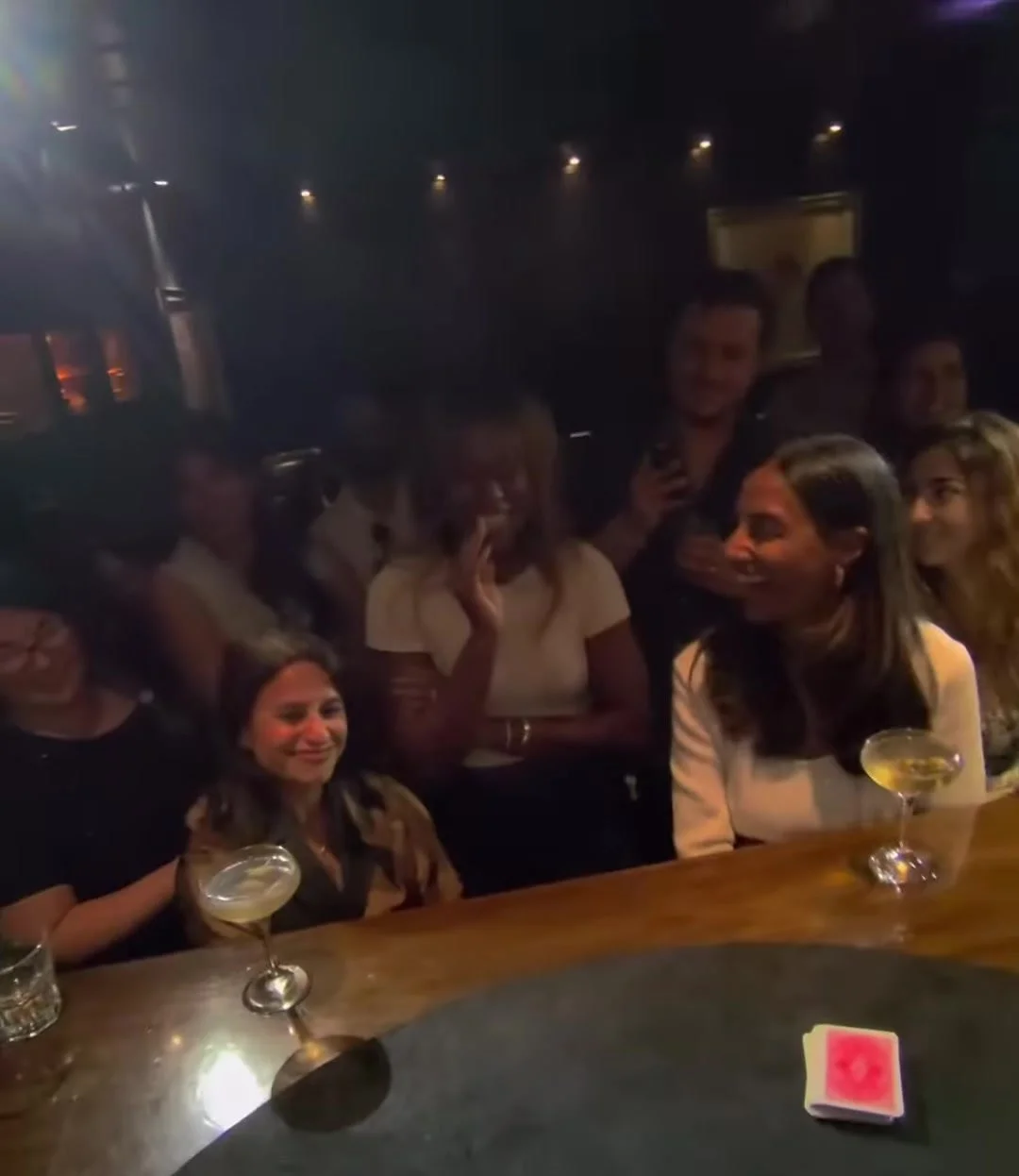 Guests react with delight at a bar-side close-up card moment during a hospitality activation.