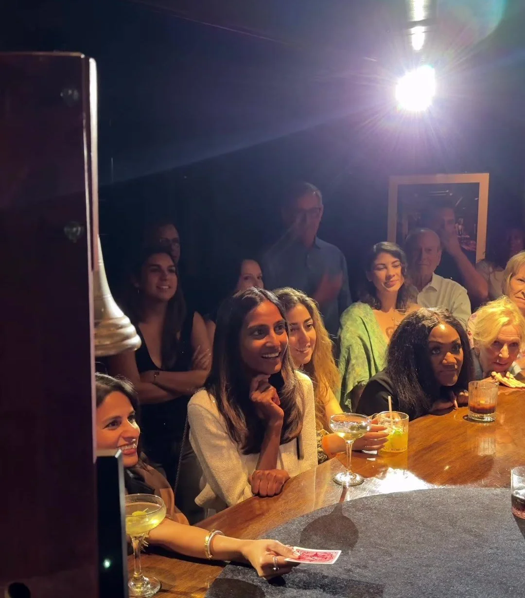 Guests leaning on a bar watching HUBB's close-up sleight of hand, one holding up a playing card.