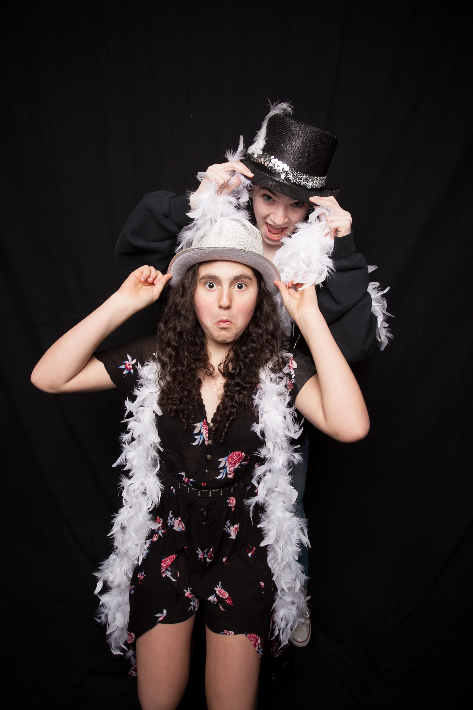 Two girls posing with feather boas and hats against a black backdrop for a bar or bat mitzvah photo booth lounge in Portland.