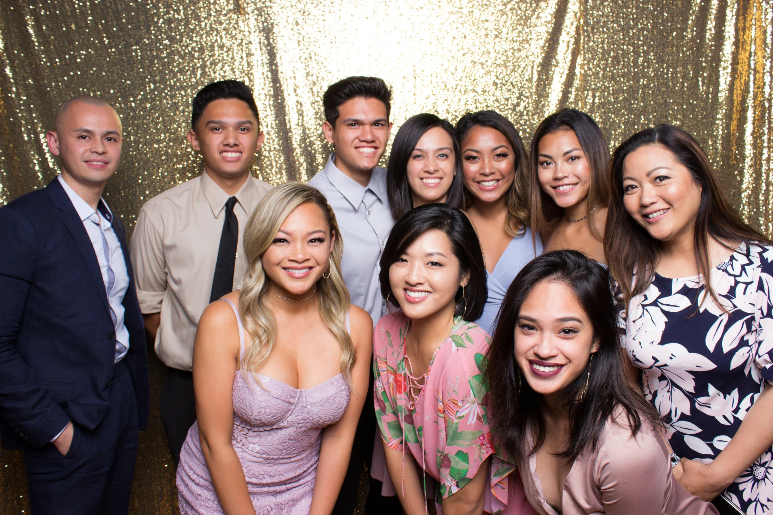 A large group in formal wear smiling together in front of a gold sequin backdrop for the 4-hour Deluxe Photo Lounge package.