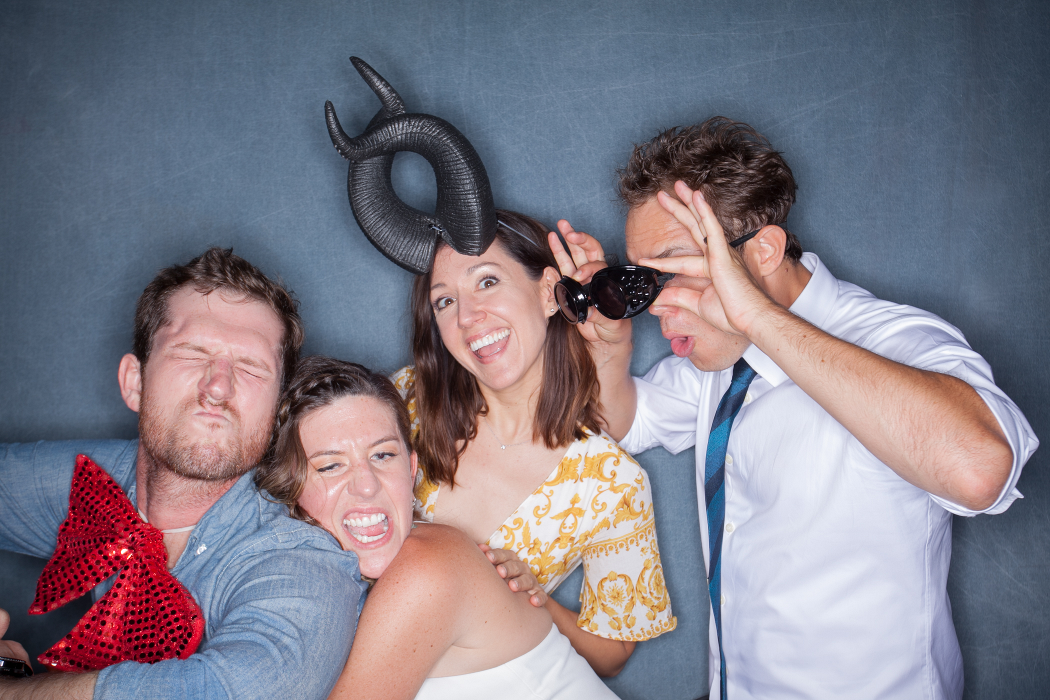 Four guests making funny faces and wearing horns and bow props against a slate gray backdrop for the 2-hour Party Box package.