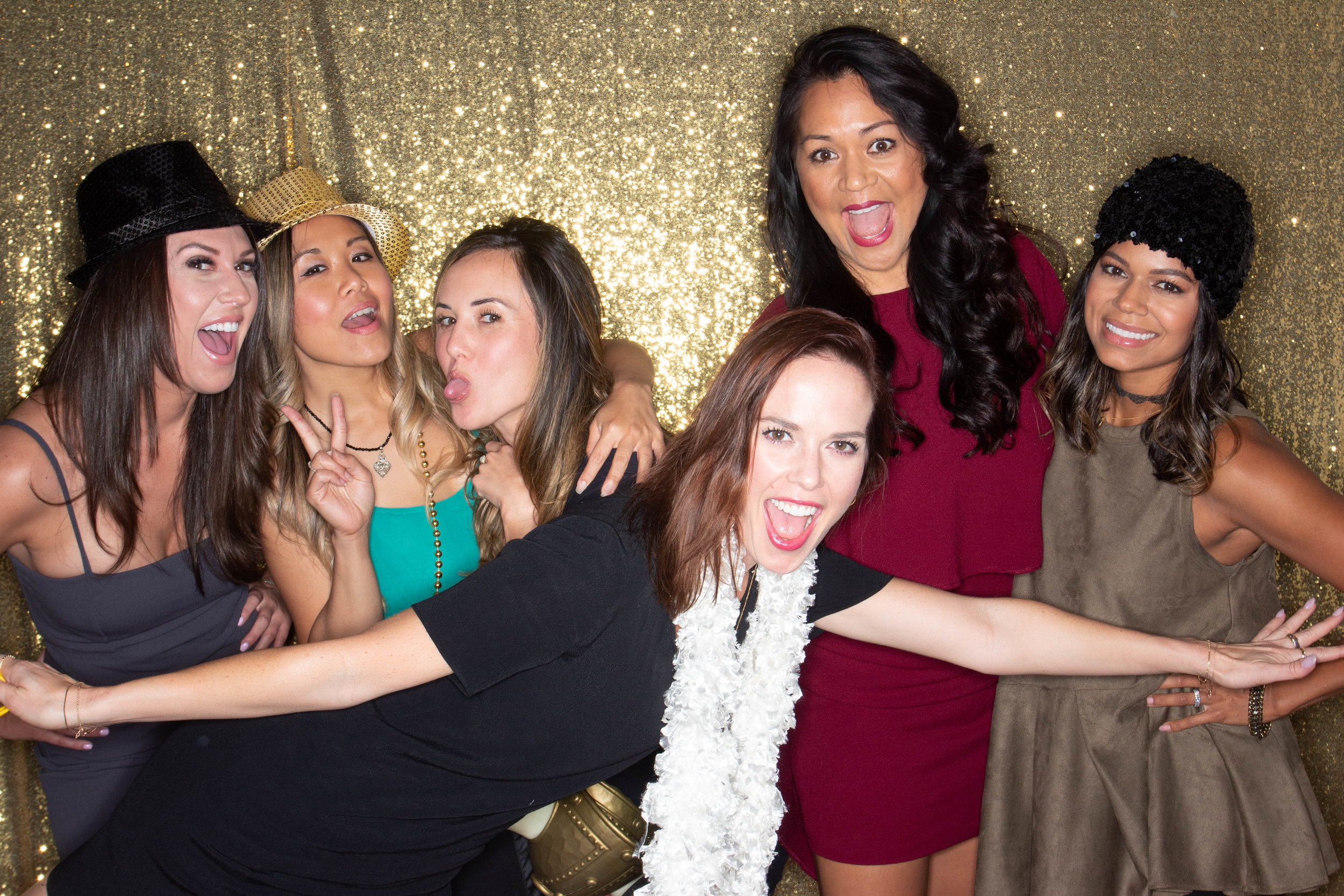 A group of women in stylish outfits and hats posing in front of a gold sequin backdrop for the 3-hour Party Box Plus photo booth package.