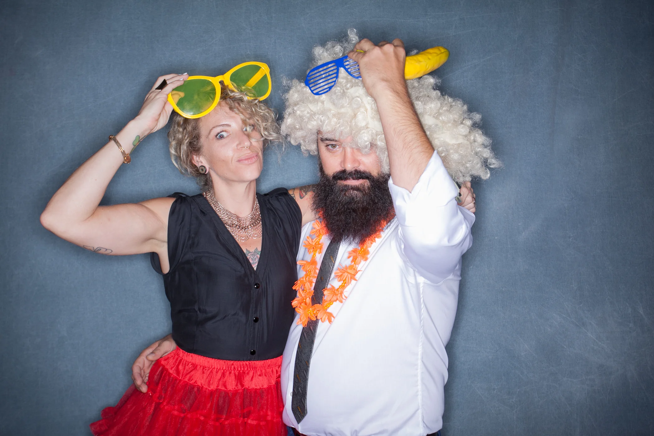 A man and woman wearing funny wigs, oversized glasses, and props for the Birthday Party Box photo booth package.
