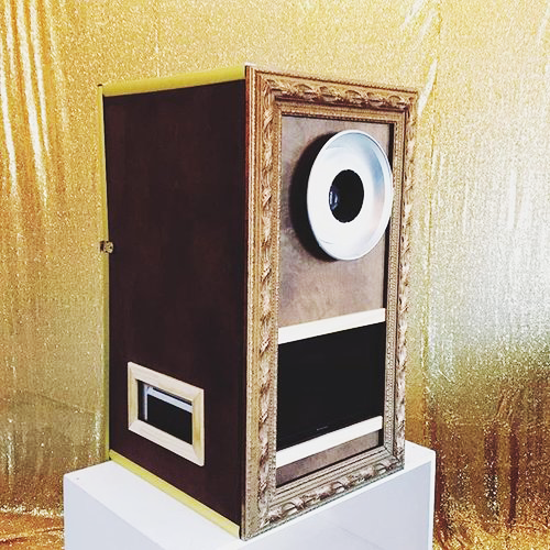 Vintage-style wooden touchscreen photo booth with built-in flash ring light and gold sequin backdrop.