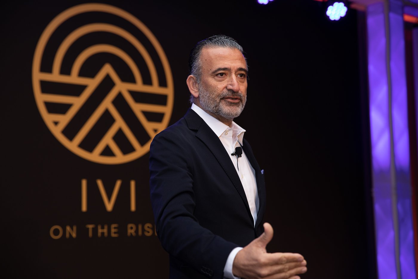 Professional event photographer capturing a keynote speaker presenting in front of a company branded backdrop.