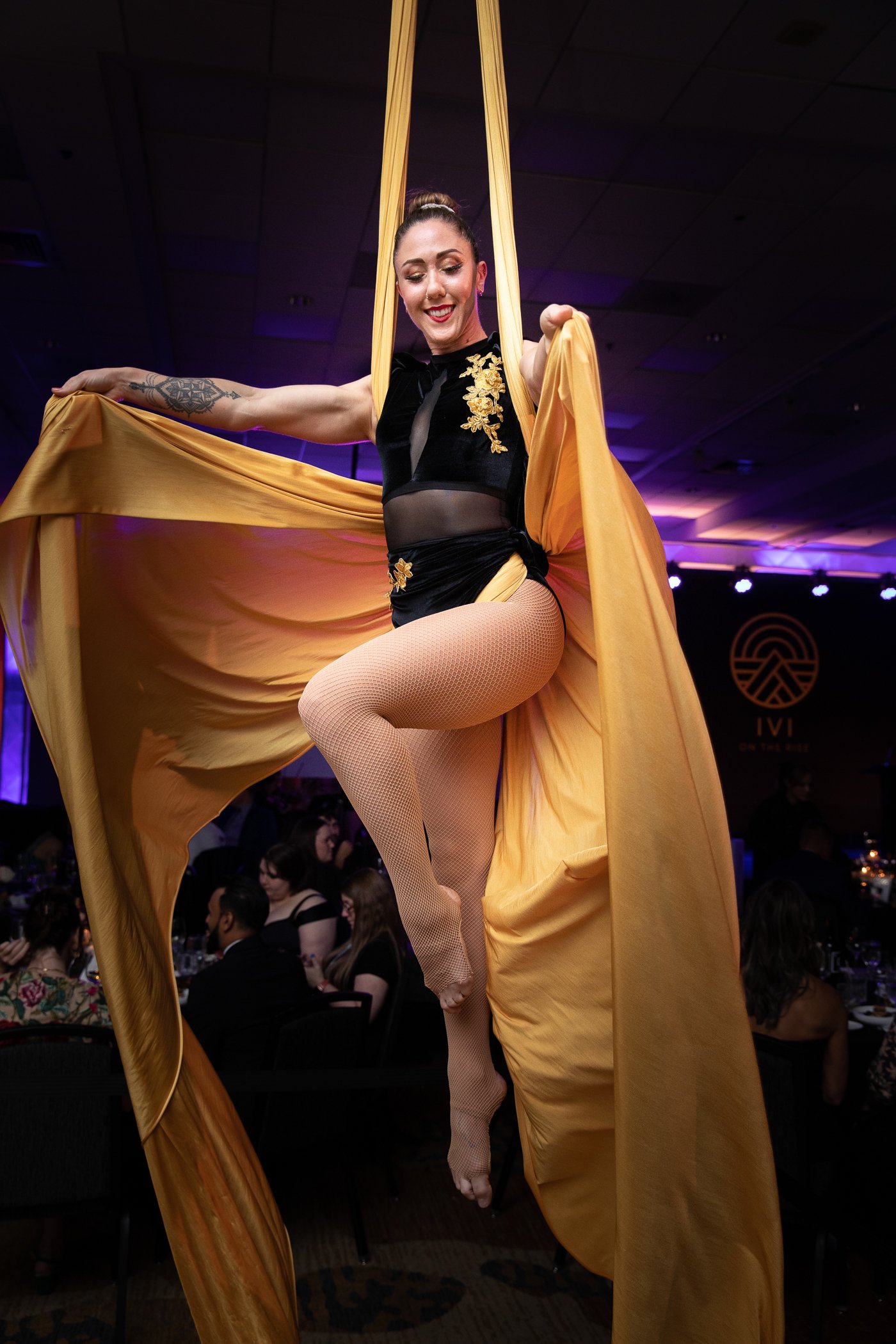 Professional event photography of an aerial silk performer in a gold costume at a corporate gala in Portland.