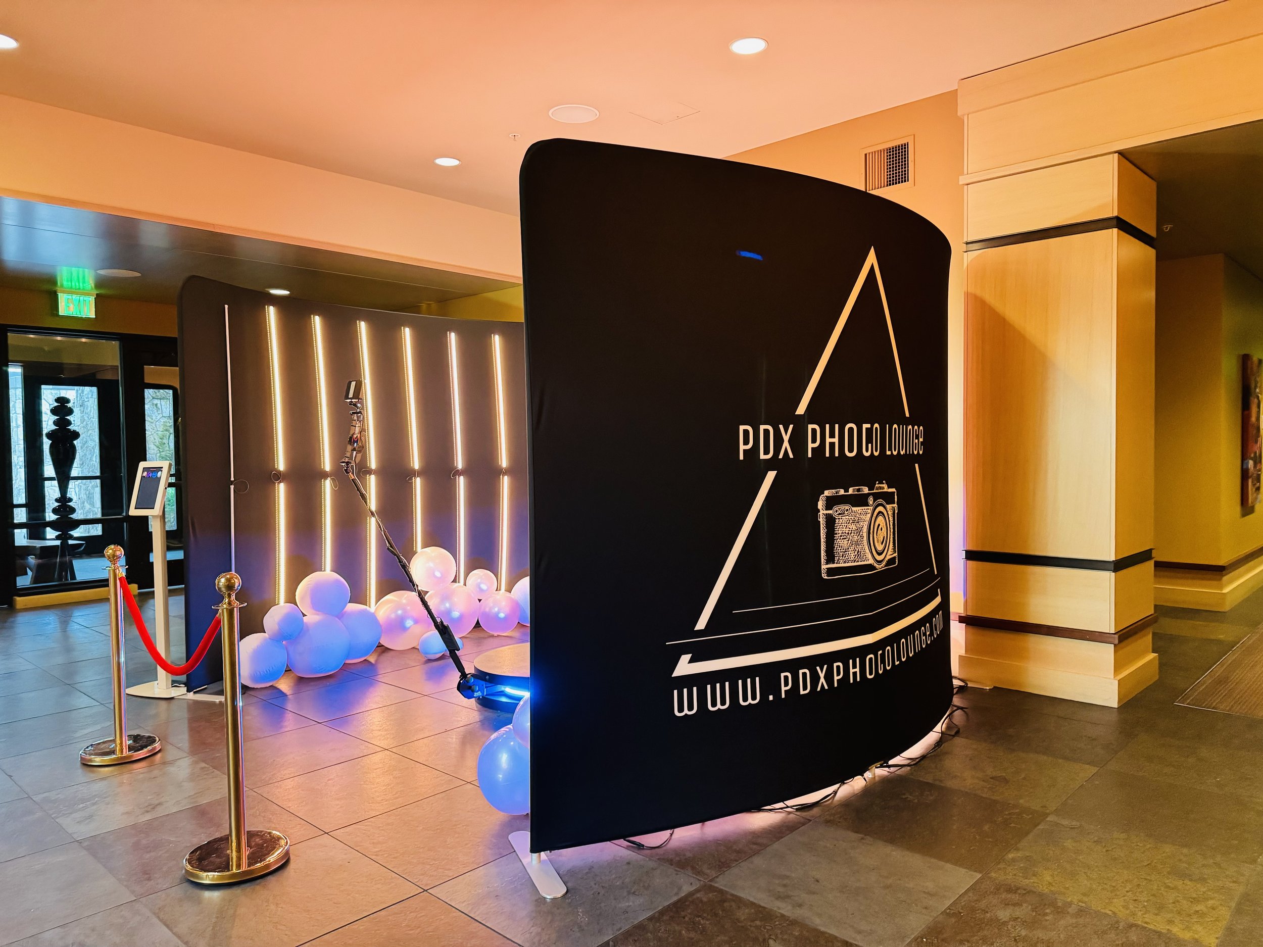 PDX Photo Lounge 360 photo booth setup featuring custom branded enclosure, stanchions, and LED lighting at an event venue in Portland.