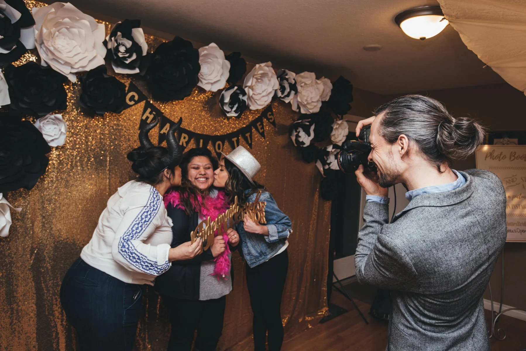 Professional photographer taking photos of guests at a PDX Photo Lounge setup with a gold glitter backdrop.