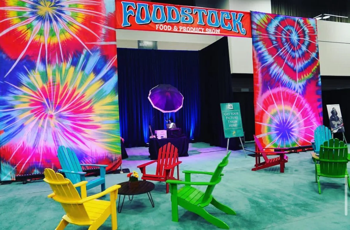 Vibrant tie-dye event backdrop and colorful lawn chairs set up for the Foodstock food and product show photo booth activation.