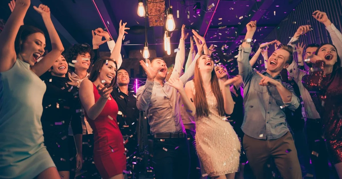 A corporate holiday party with a group of people dressed nicely and gathered for a photo. Confetti flies around.