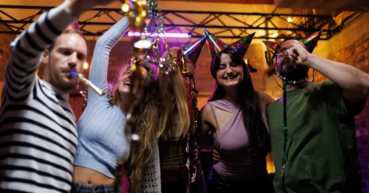 A group of friends gathered together playing with their party favors, including streamers, hats, and noise makers.