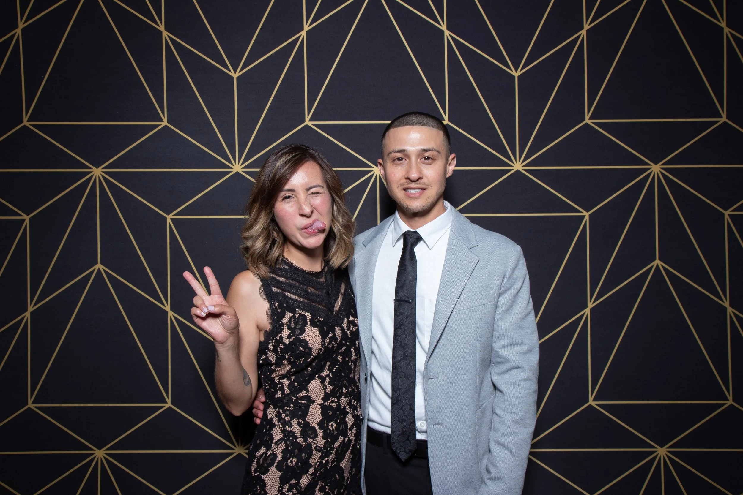 A couple making playful faces in front of a black and gold geometric backdrop for the 2-hour Touch Photo Booth package.