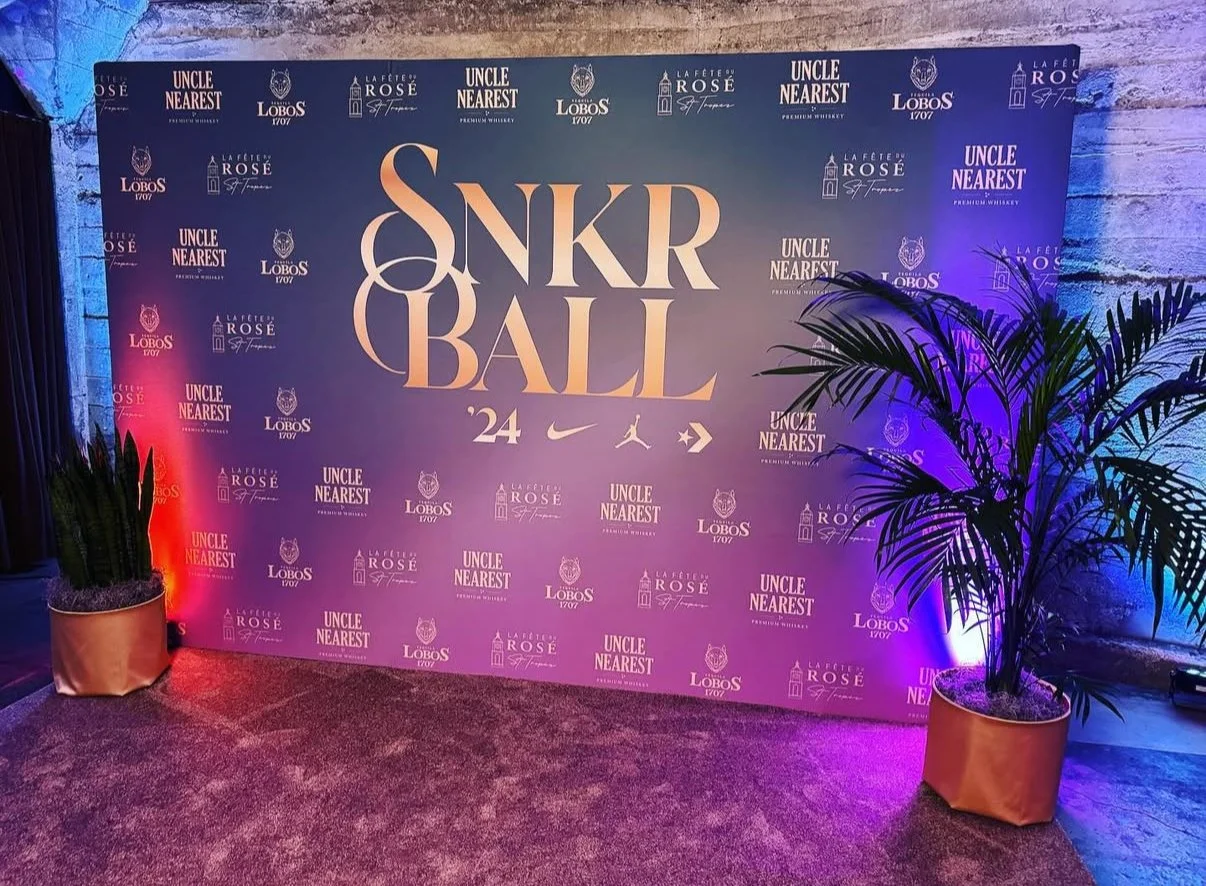Custom SNKR BALL step and repeat media wall backdrop with purple lighting and potted palm plants for a branded event.