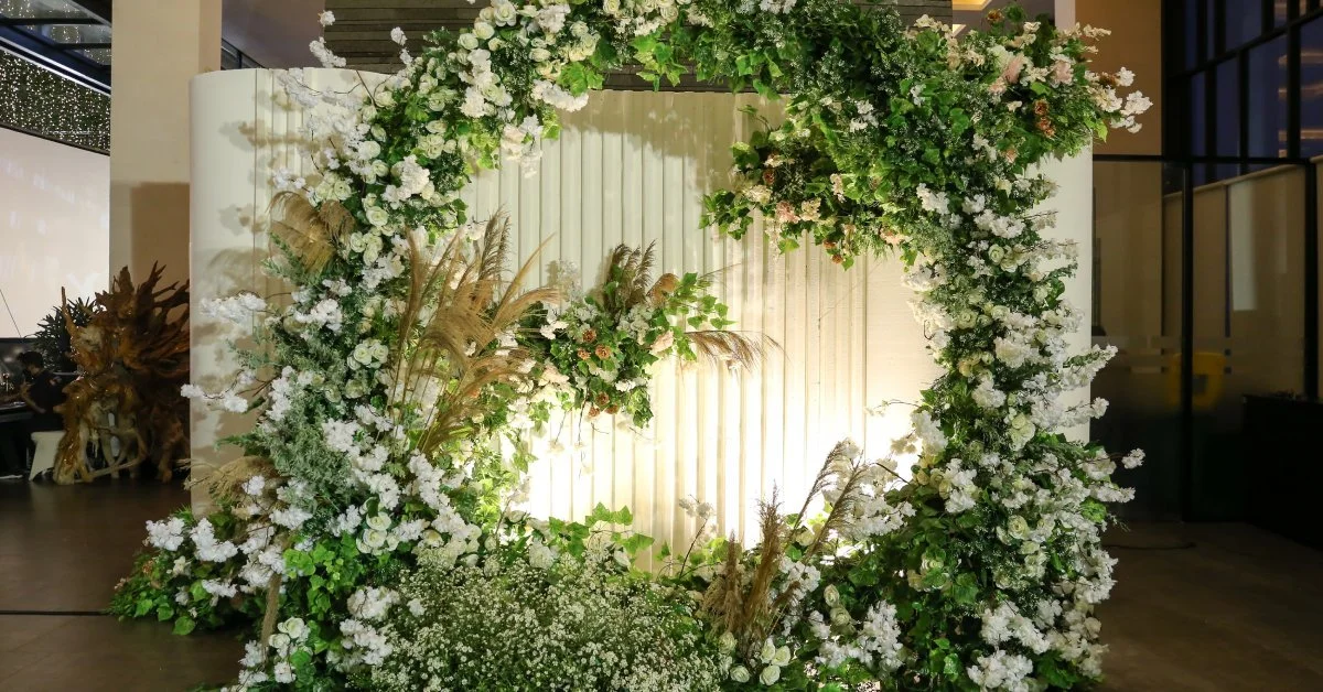 A beautiful, floral arrangement on a white, textured backdrop set up for a photo booth at a wedding reception.