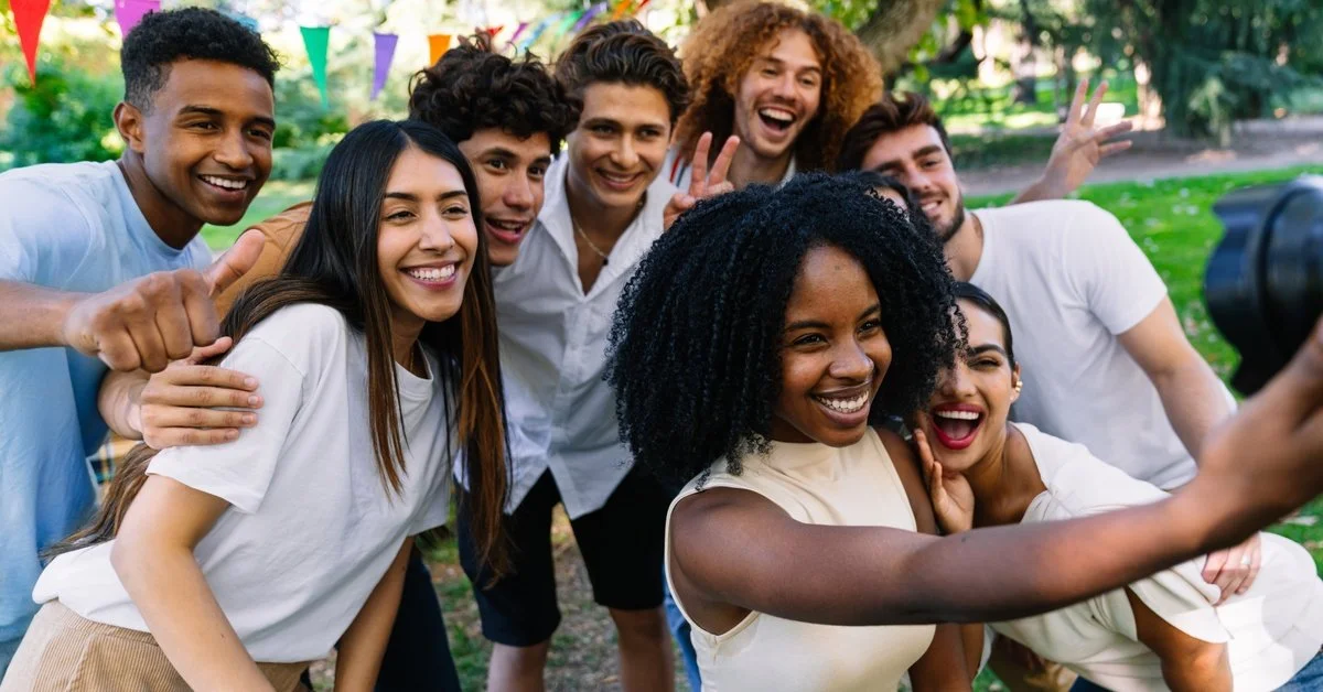 A group of people at an event taking a photo. The Black woman in the front holds the camera and other people smile.