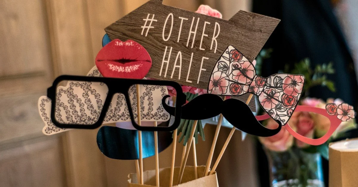 A table set up with photo booth props in a wedding theme. The props are sitting in a brown paper bag.