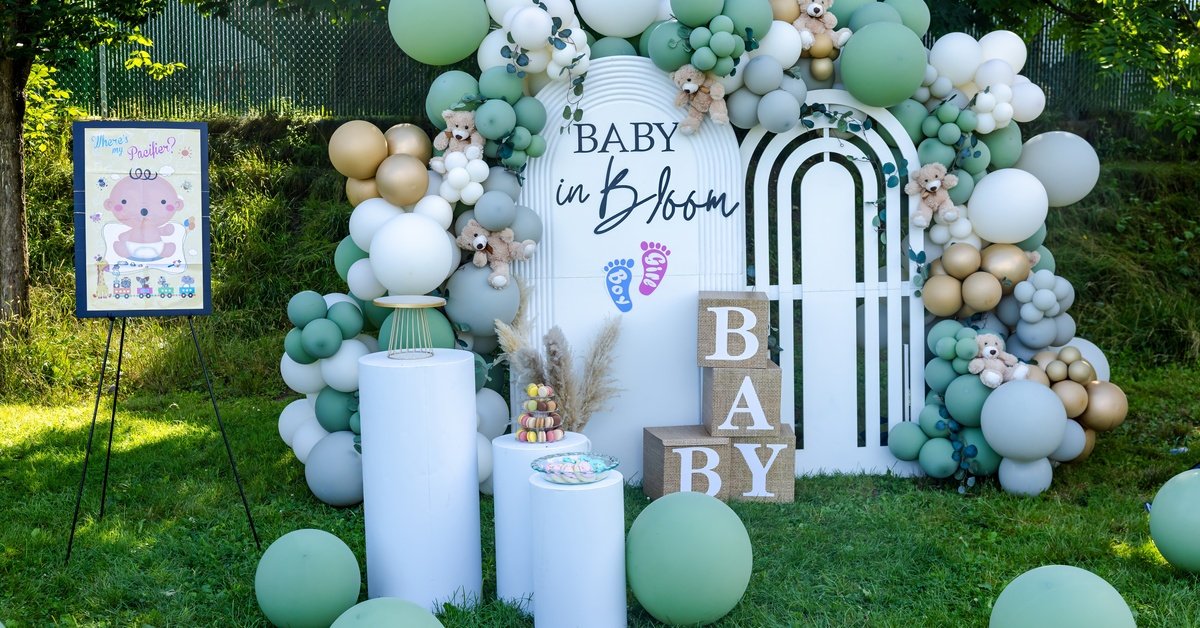 A baby shower photo opportunity setup complete with green, gold and white balloon arches and baby signs.