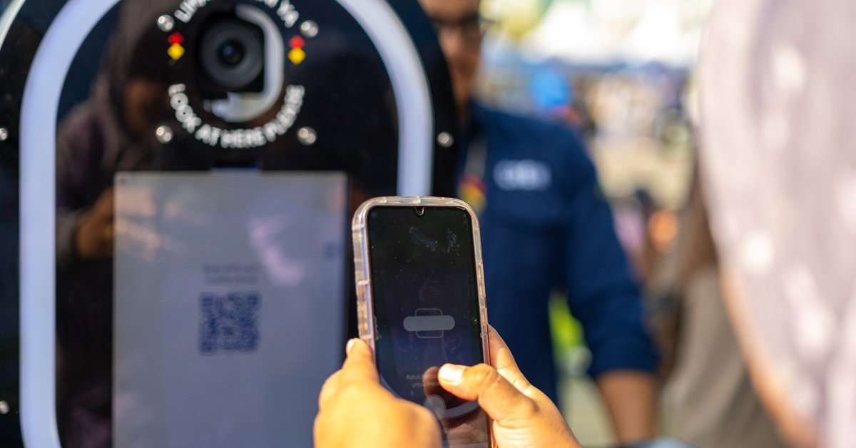 An event guest stands at the photo booth station taking a photo of a QR code with their phone to retrieve their images.