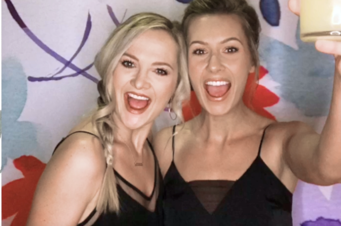 Two excited women smiling and holding drinks in front of a colorful backdrop for the 2-hour Salsa Photo Booth package.