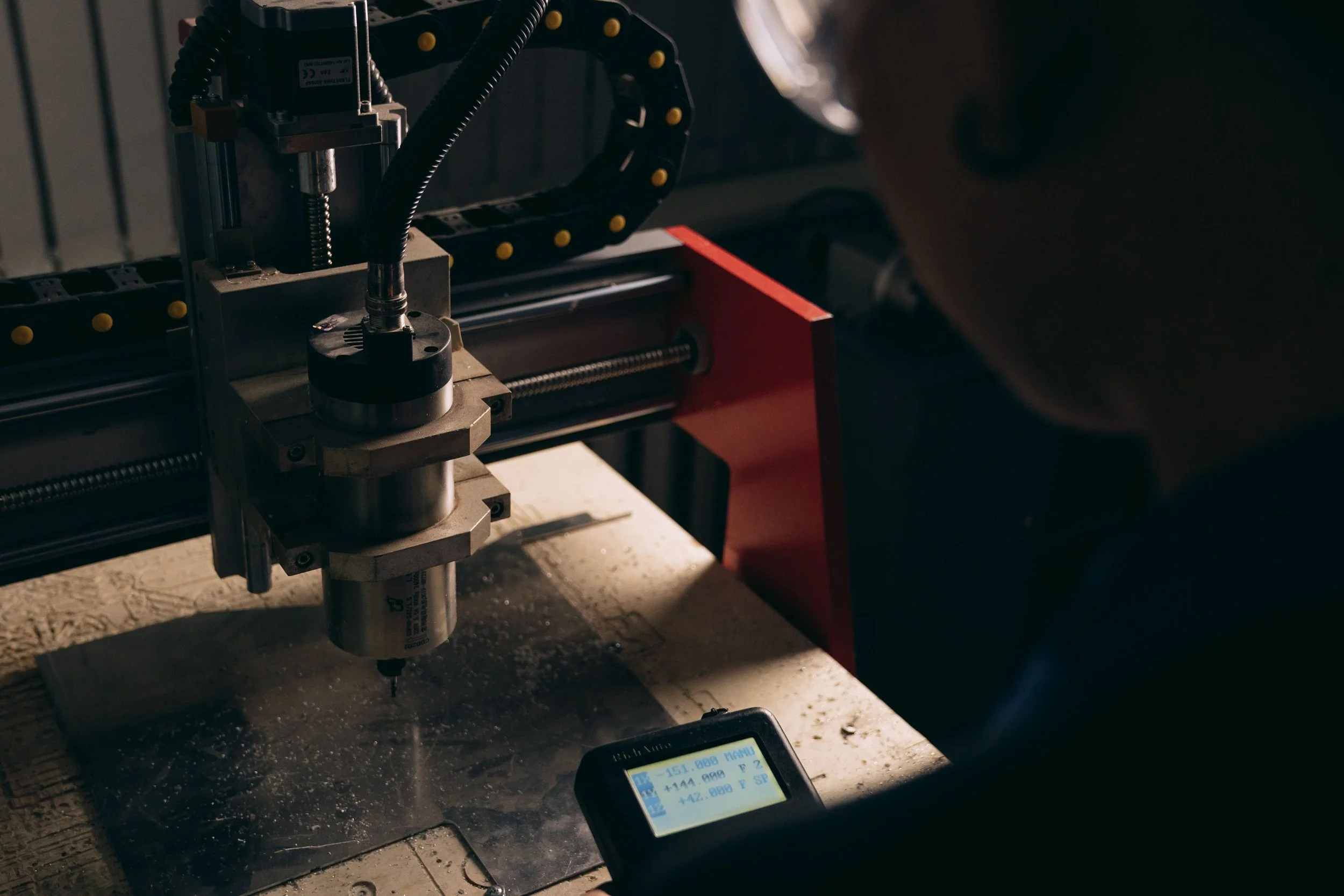 A close-up of a CNC milling machine working on a metal part, with a person operating it and a digital screen displaying measurements.