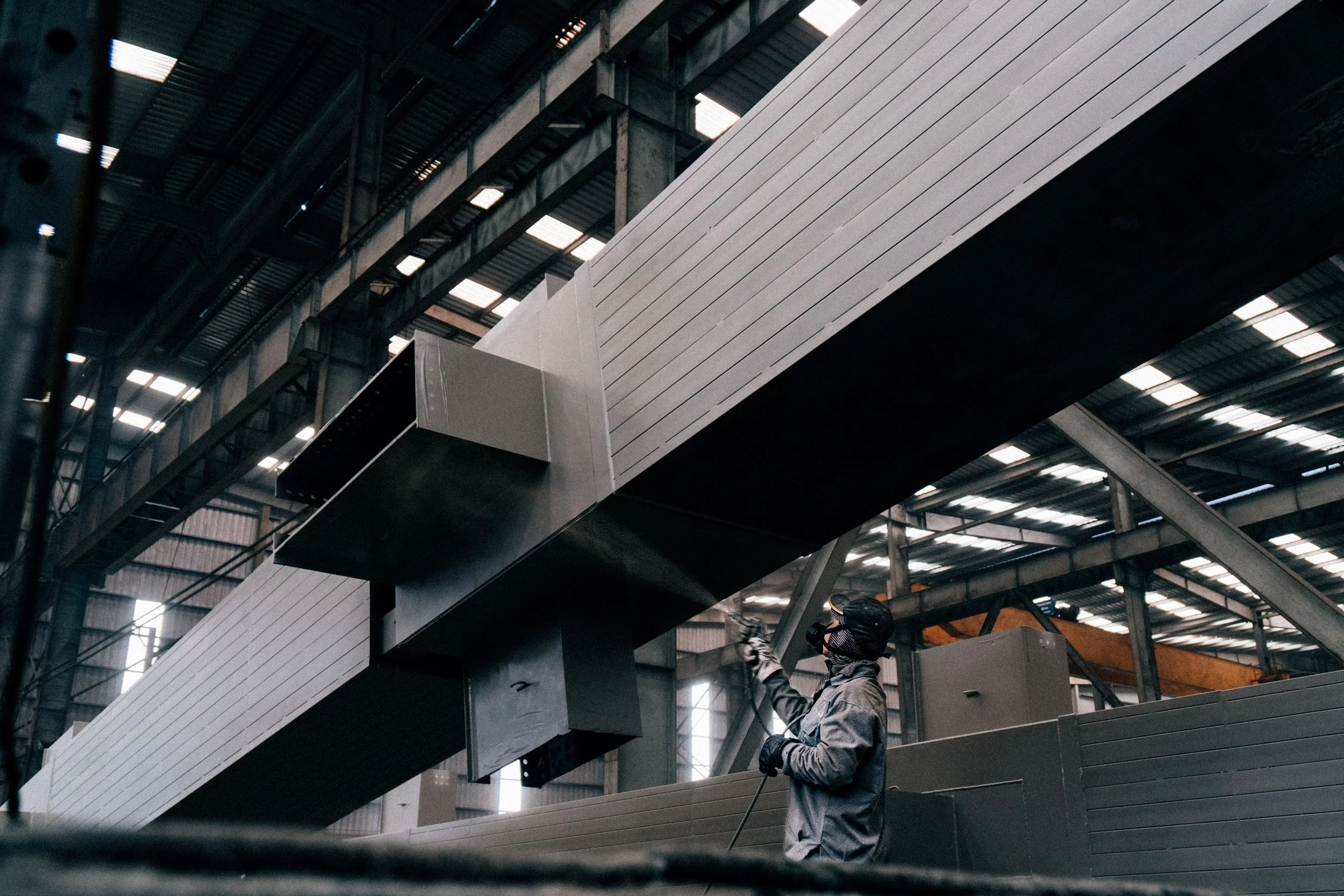 Workers cleaning or inspecting the interior structure of a large modern building with metal beams, stairs, and ventilation systems.